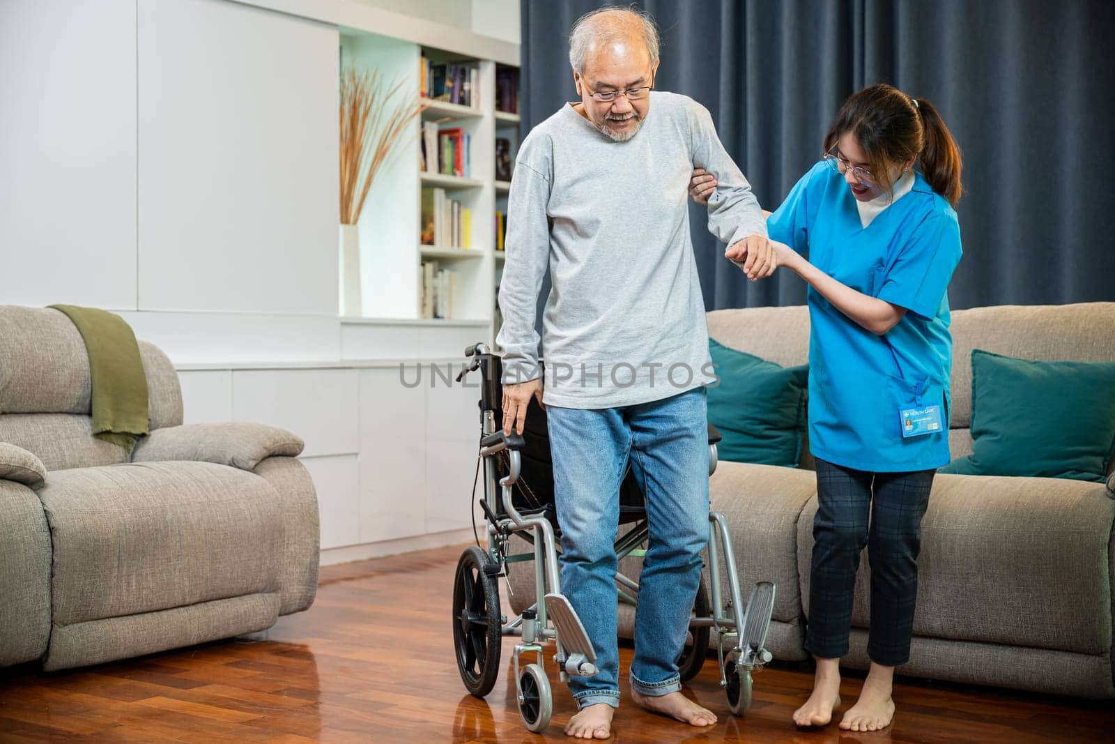 Doctor support old man to getting up to exercise, help handicapped elderly stand up, Asian woman nurse helping senior man patient get up from wheelchair for practice walking at home, physical therapy