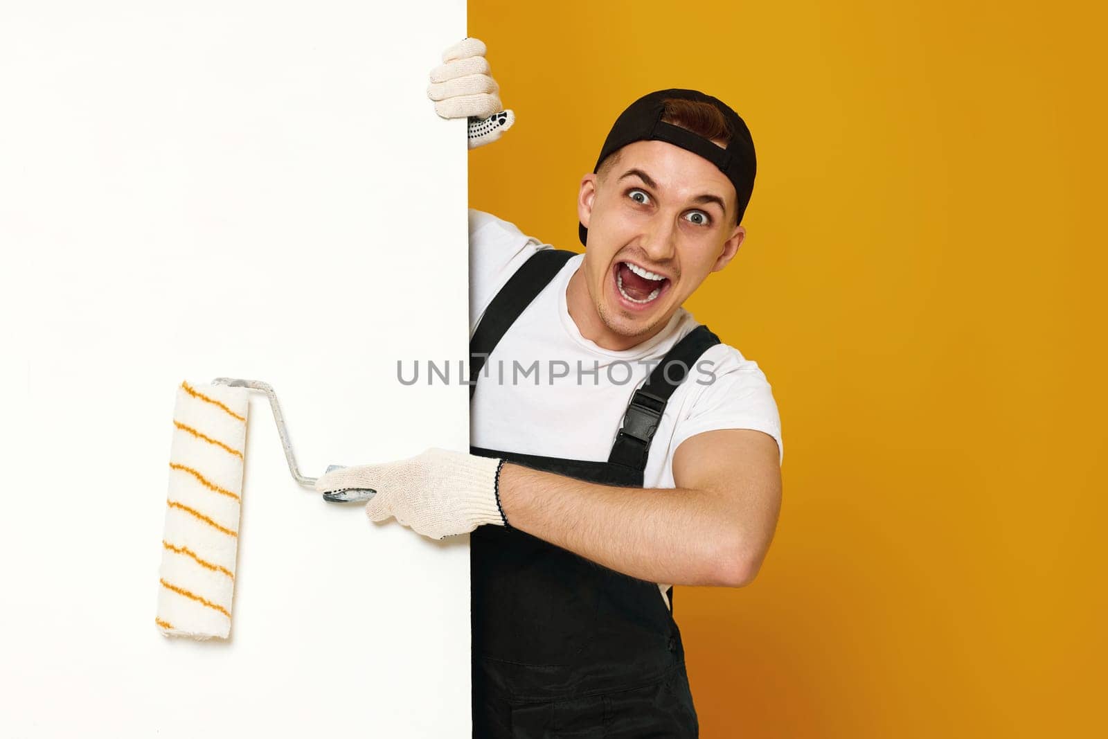 surprised young man in working clothes painting white walls in the room. copy space for text