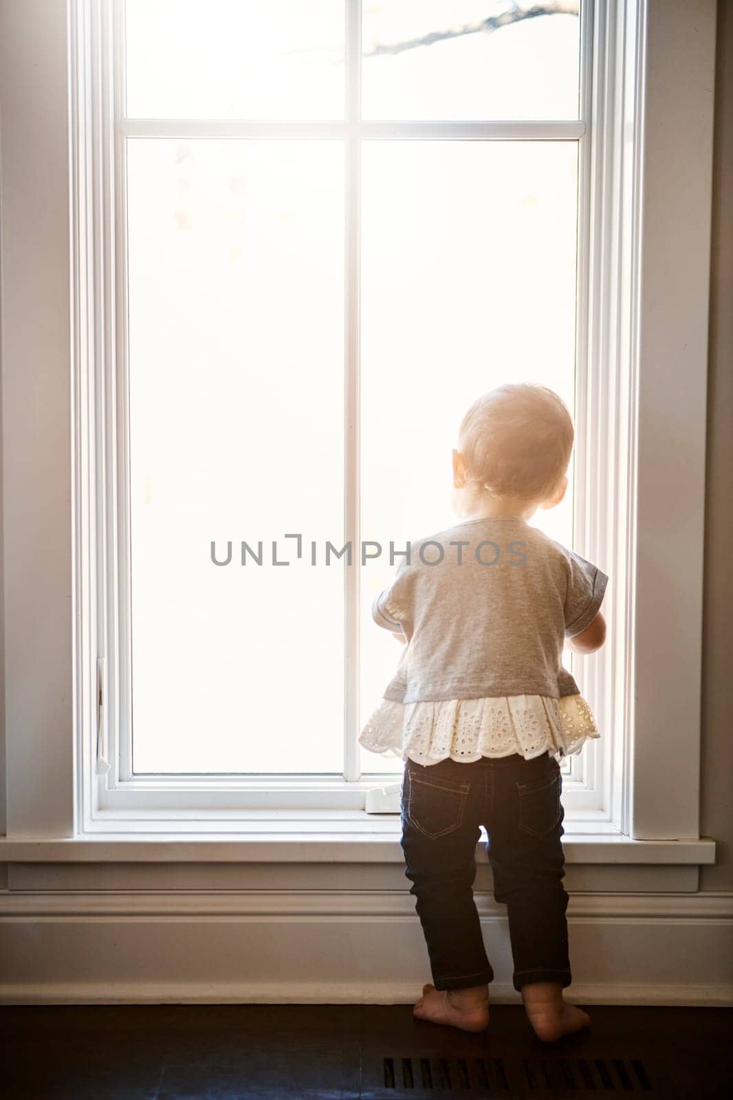 The world is yours little one. Rearview shot of an adorable little girl looking out of the window at home. by YuriArcurs