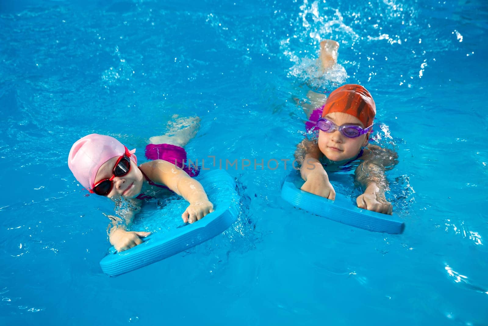 Two little kids learning how to swim in swimming pool using flutter boards by Mariakray