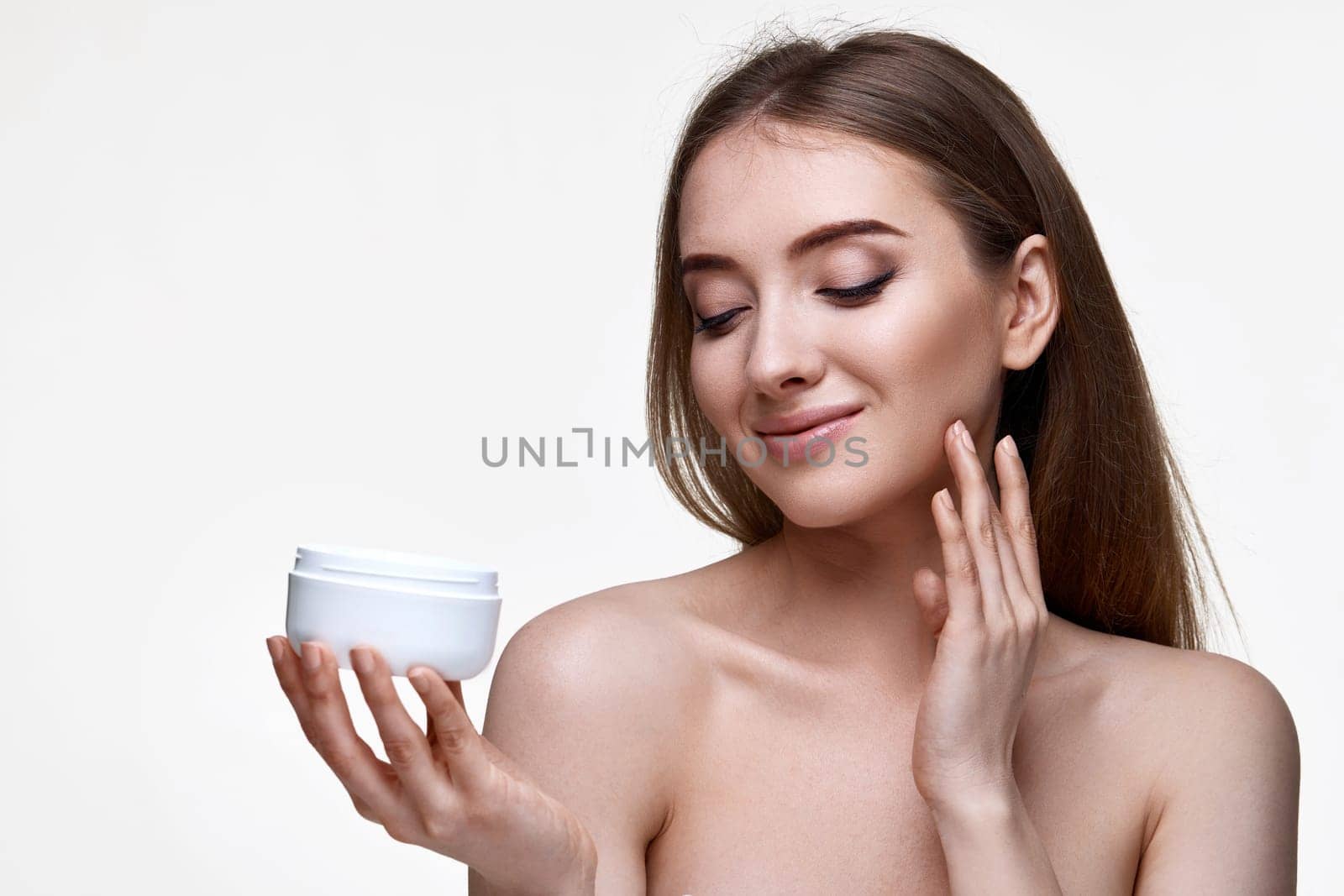 beautiful happy young woman applying skin care cream on her face on white background