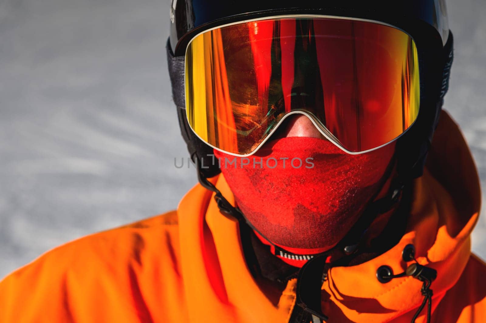 Portrait of a man with yellow eyes. Photo of a young serious sportsman in a helmet and ski goggles in his hands, against the backdrop of a snowy hill.