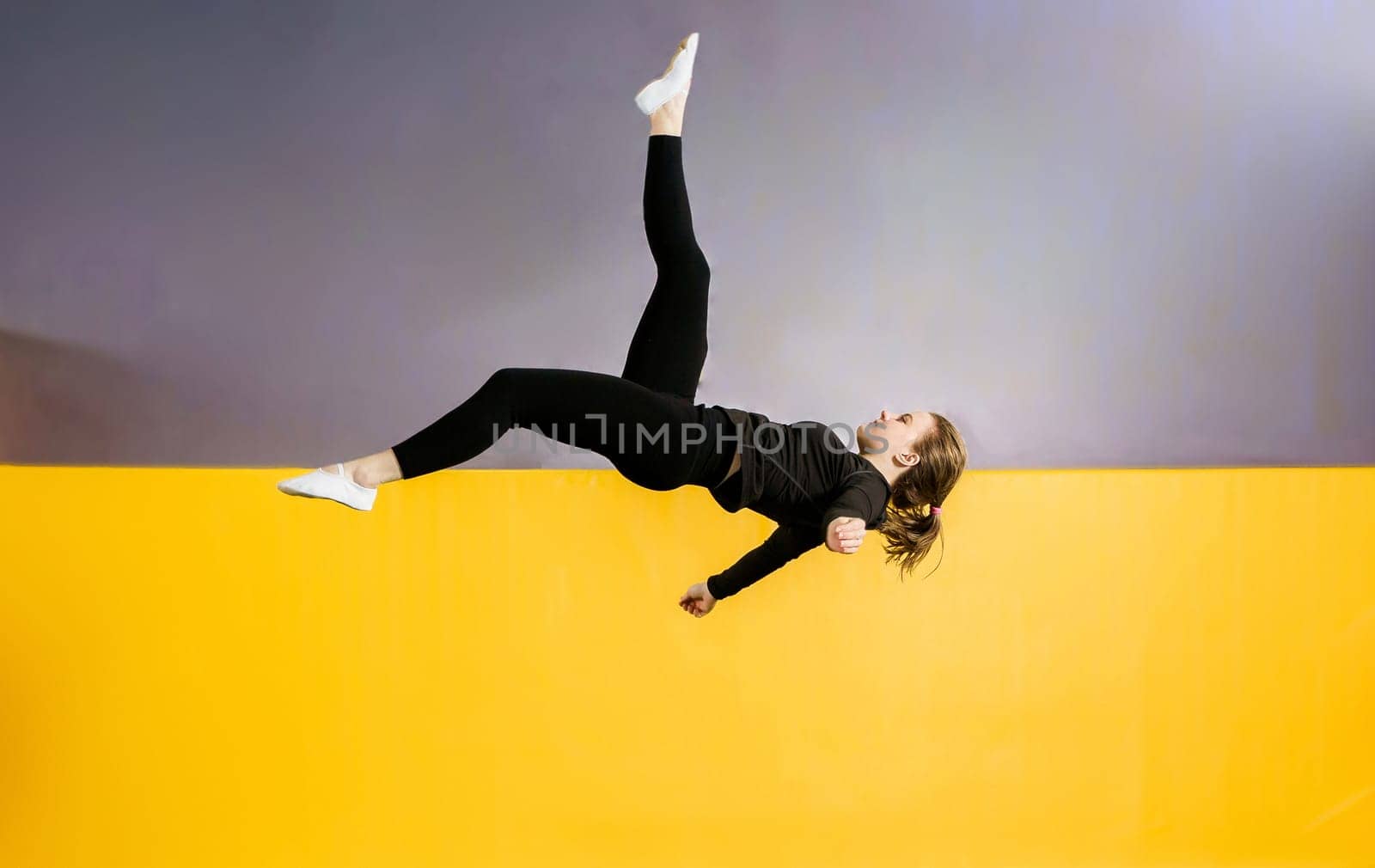 Young woman amateur acrobatic athlete jumping and exercising on a trampoline indoors, modern hobby and fitness concept by Mariakray