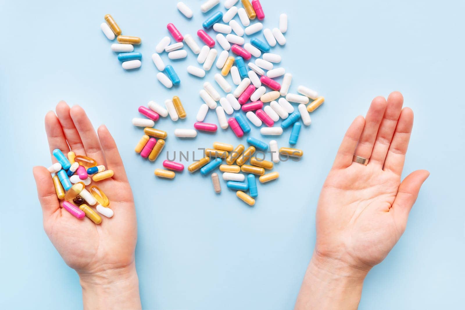 The girl holds a handful of bright vitamins, nutritional supplements and medicines in her palms on a blue background. Concept of medicine and healthcare