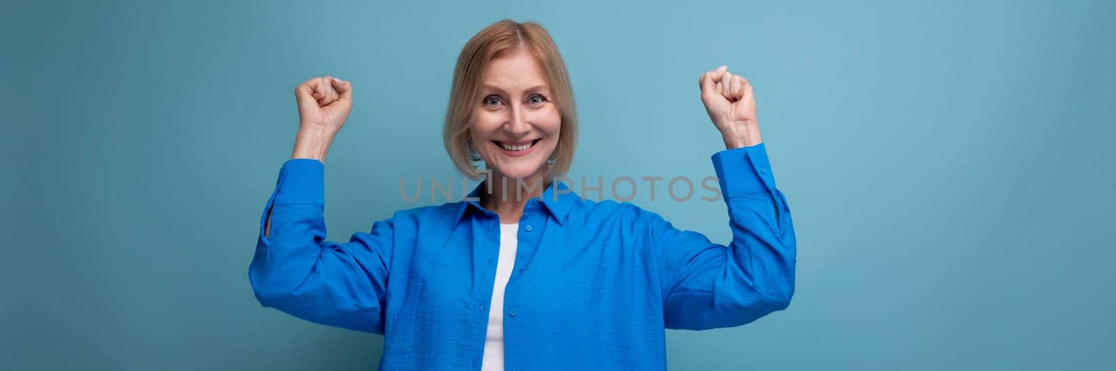 close-up of a joyful middle aged woman in a blue shirt on a blue background with copy space by TRMK