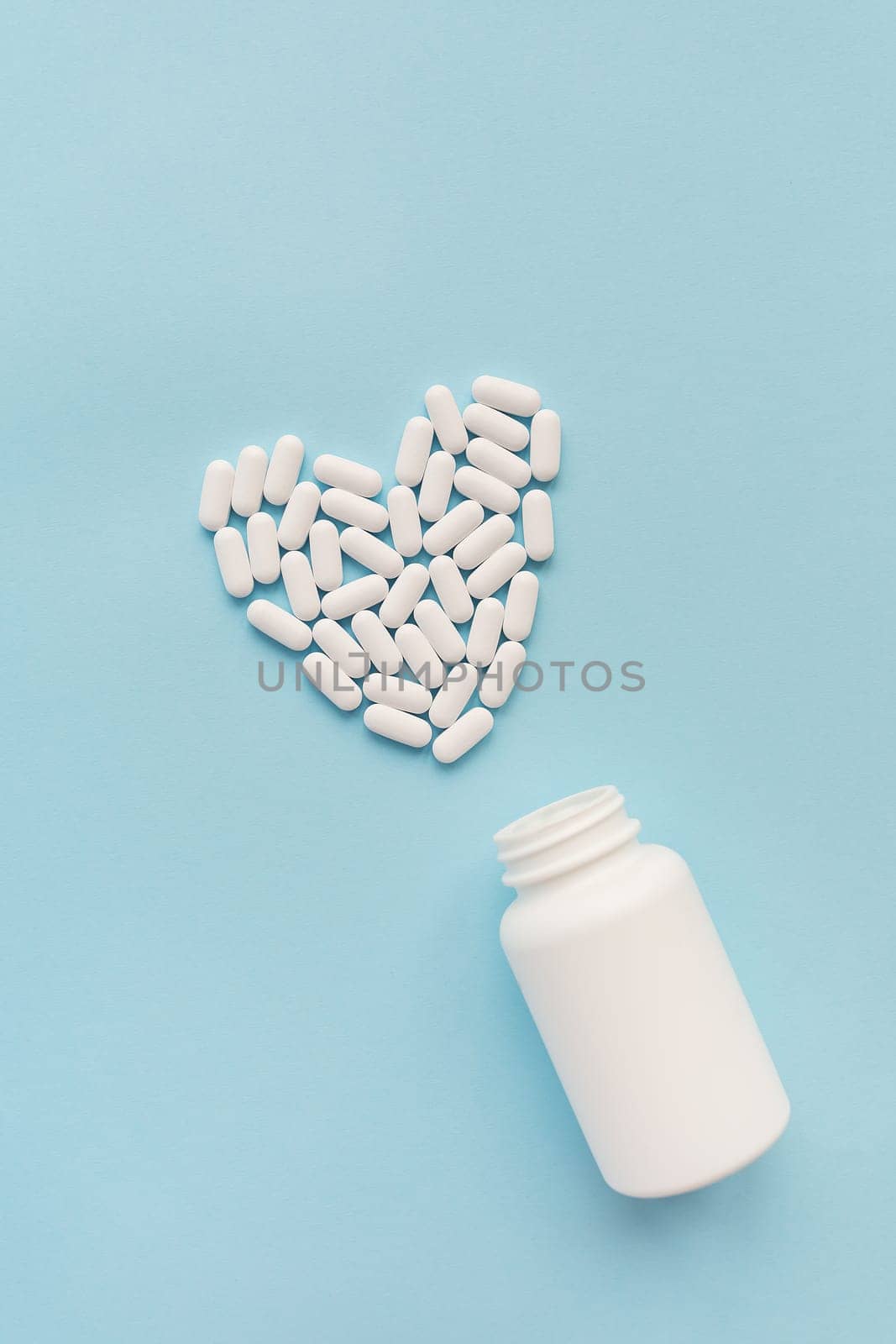 White pills in the shape of a heart came out of a jar on a blue background, health and heart problems together with a plastic jar. The concept of medicine and health care. Place for writing. by sfinks