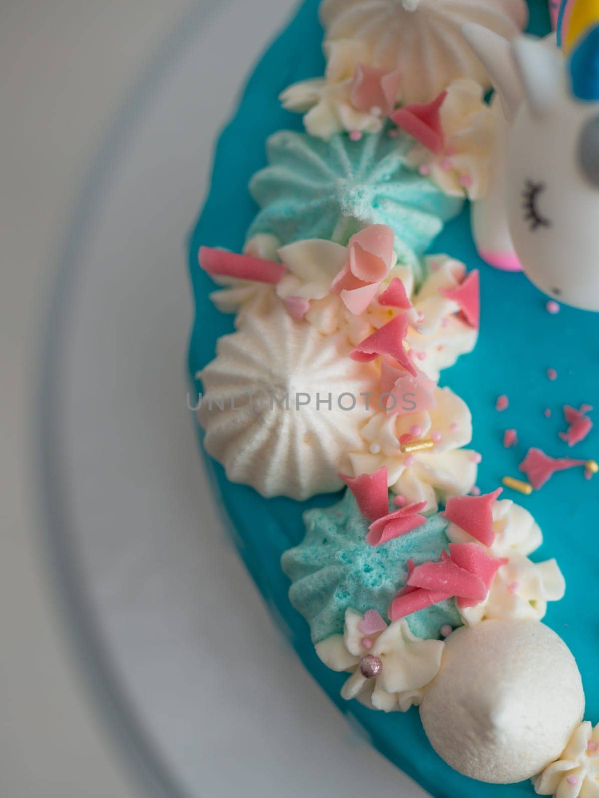 studio shot of chocolate frosted blue dripped icing white cup cake, unicorn , meringue and sprinkles on top