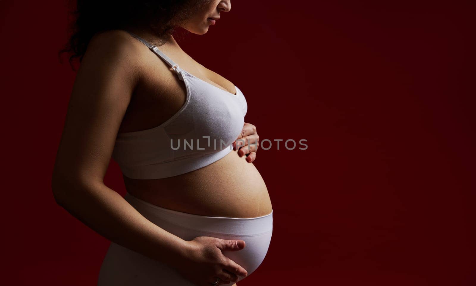 Young pregnant woman in white lingerie, caressing her belly, isolated on red background. Femininity Nudity Pregnancy by artgf