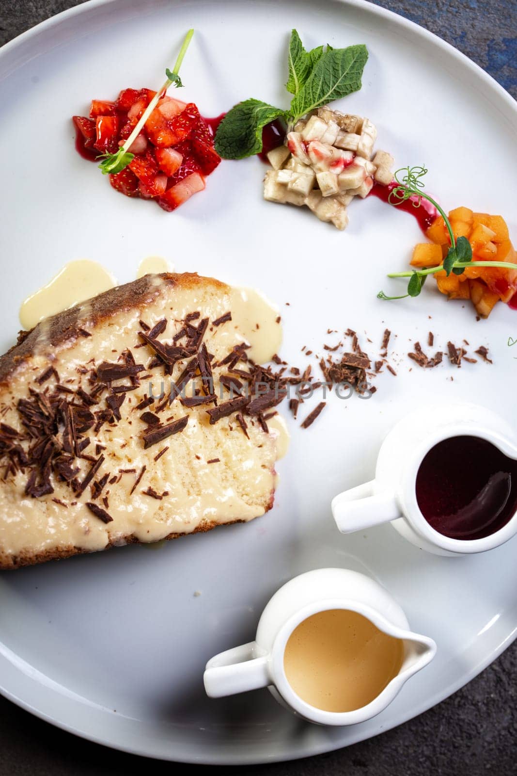 sponge dessert with chocolate chips and fruit on a white plate.