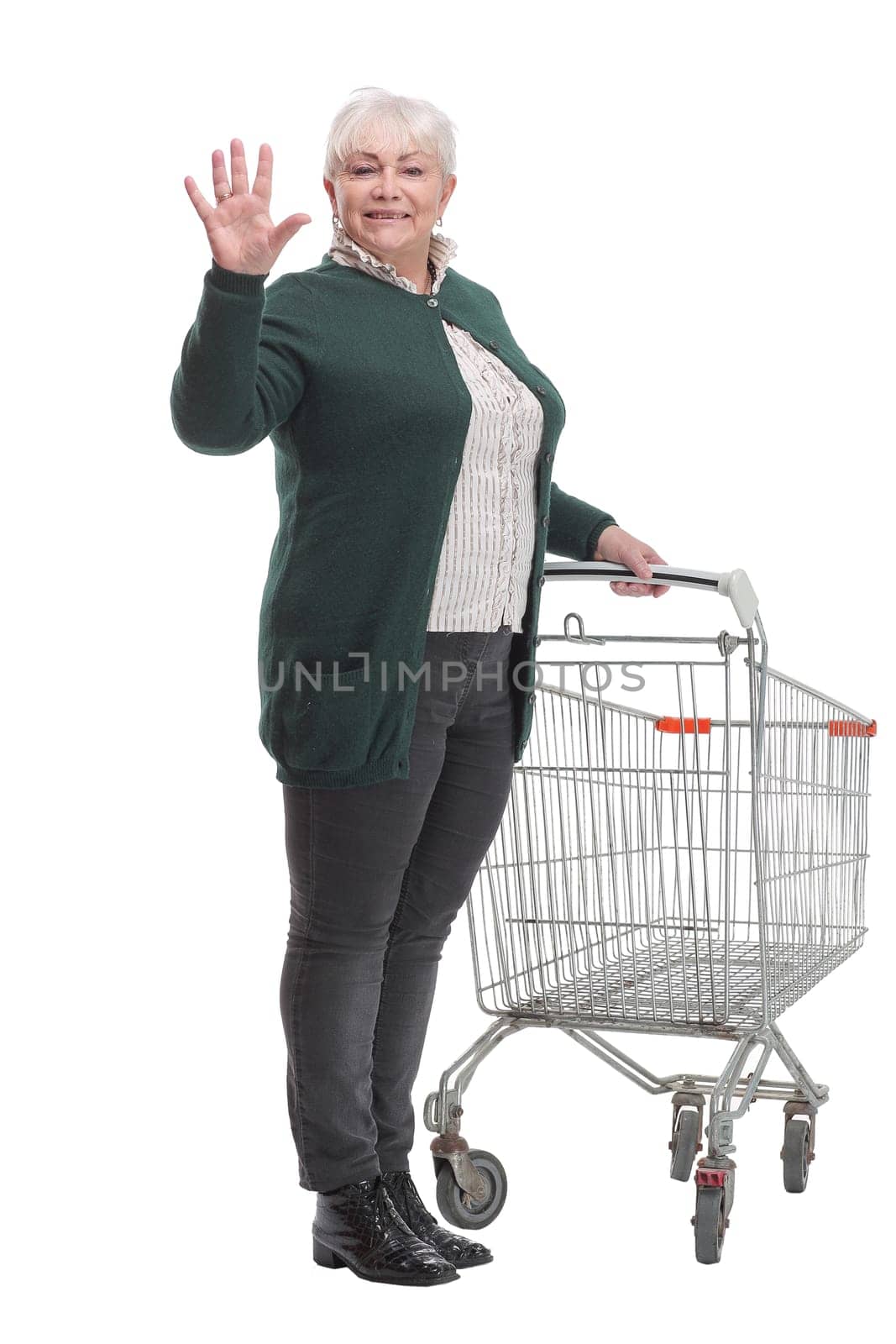 Full length shot of a senior lady waving and pushing an empty shopping cart isolated on white background