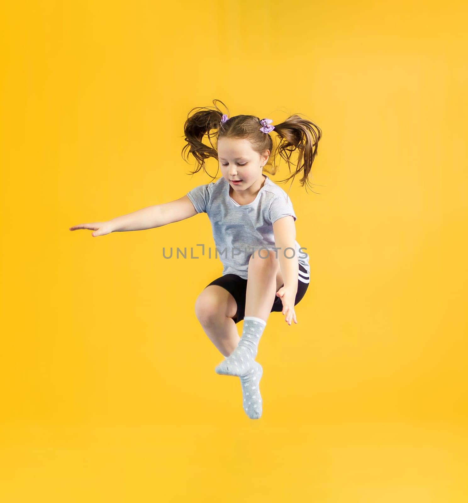 Happy little girl jumping on yellow background by Mariakray