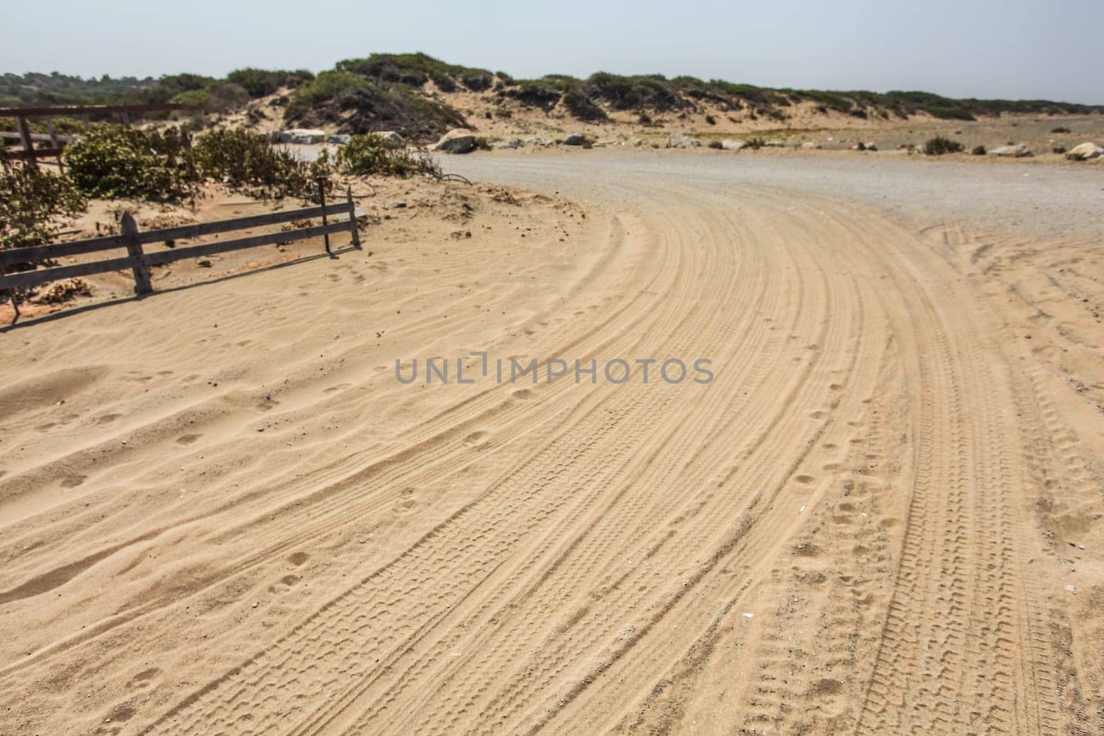 Car tire prints on a road leading to beach covered in sand.