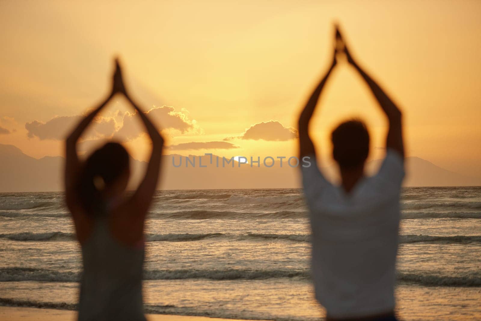 Appreciating the beauty of nature while doing yoga. Rearview shot of a couple doing yoga on the beach at sunset. by YuriArcurs