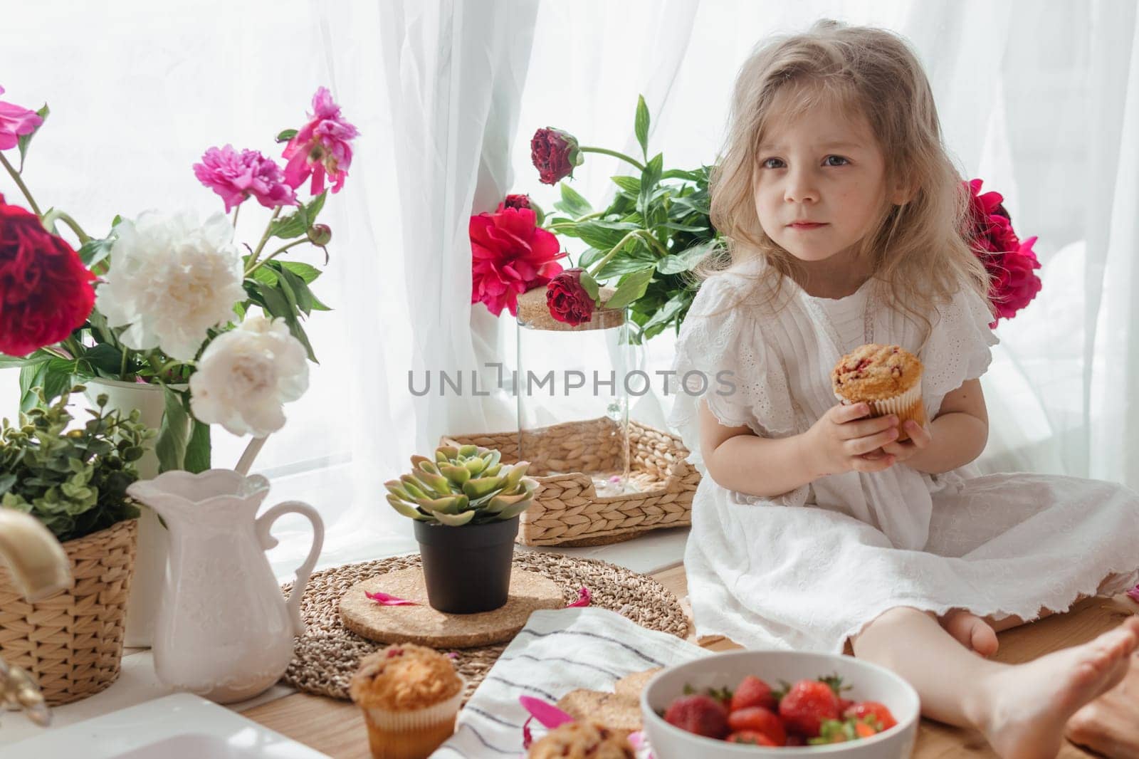 A little blonde girl on a kitchen countertop decorated with peonies. Spring atmosphere