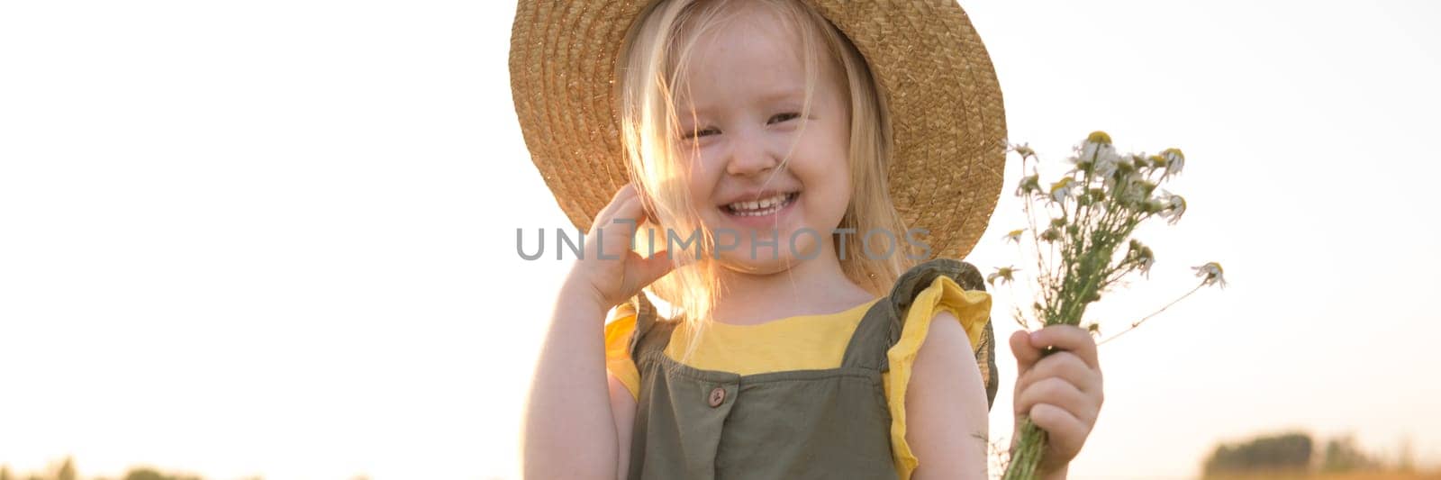 A little blonde girl in a straw hat walks in a field with a bouquet of daisies. The concept of walking in nature, freedom and an eco-friendly lifestyle. by Annu1tochka
