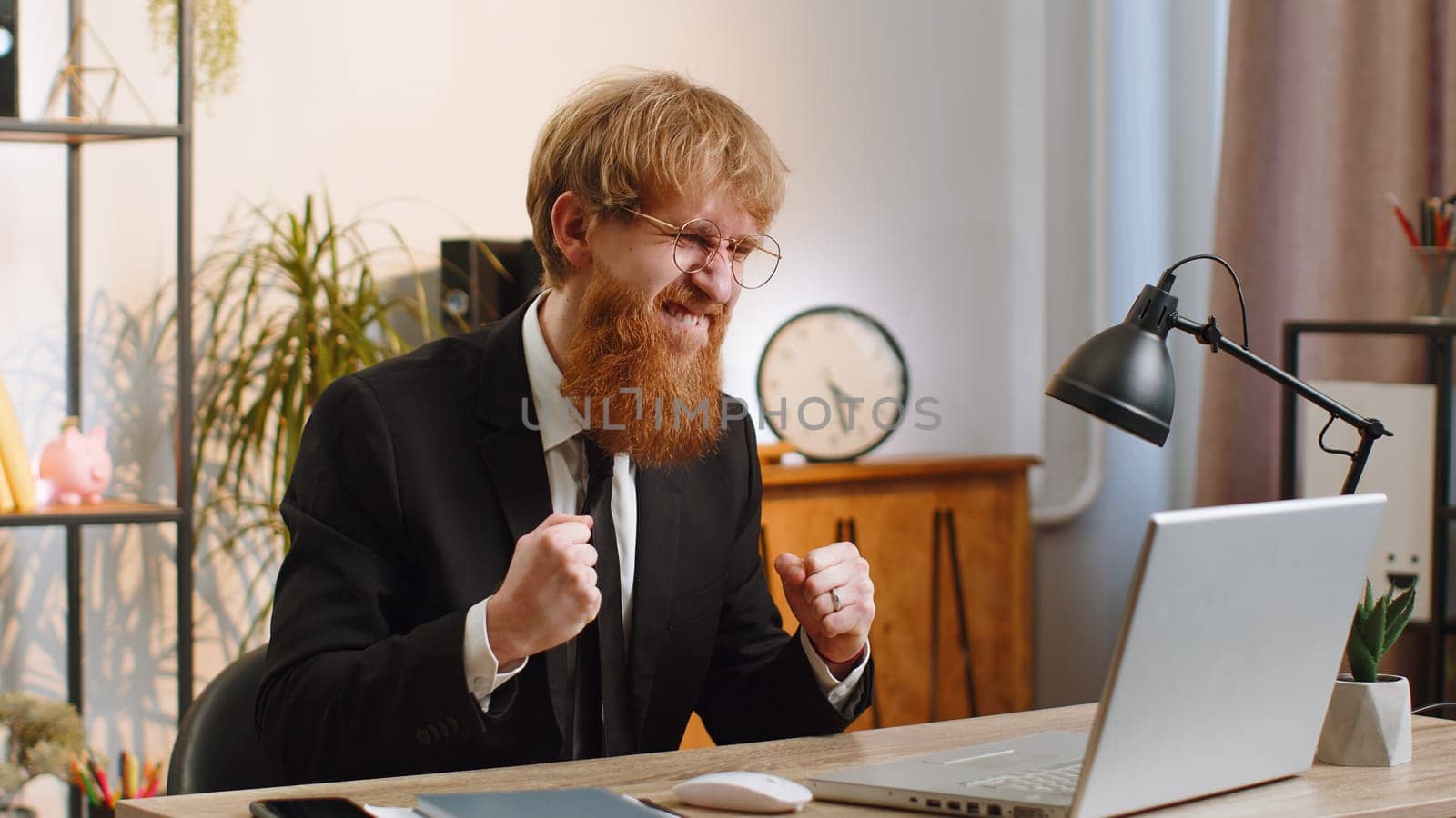 Concentrated young businessman working on laptop at home office desk typing browsing say Wow yes found out great big lottery jackpot win, good news, celebrating. Bearded manager freelancer man job