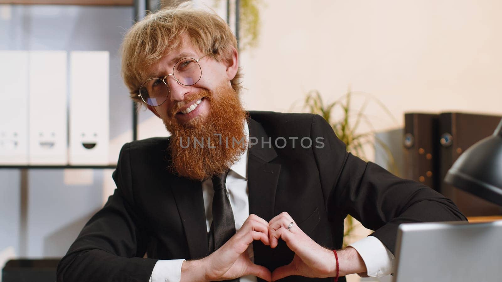 I love you. Young business man makes symbol of love, showing heart sign to camera, express romantic feelings, express sincere positive feelings at home office workplace. Charity, gratitude, donation
