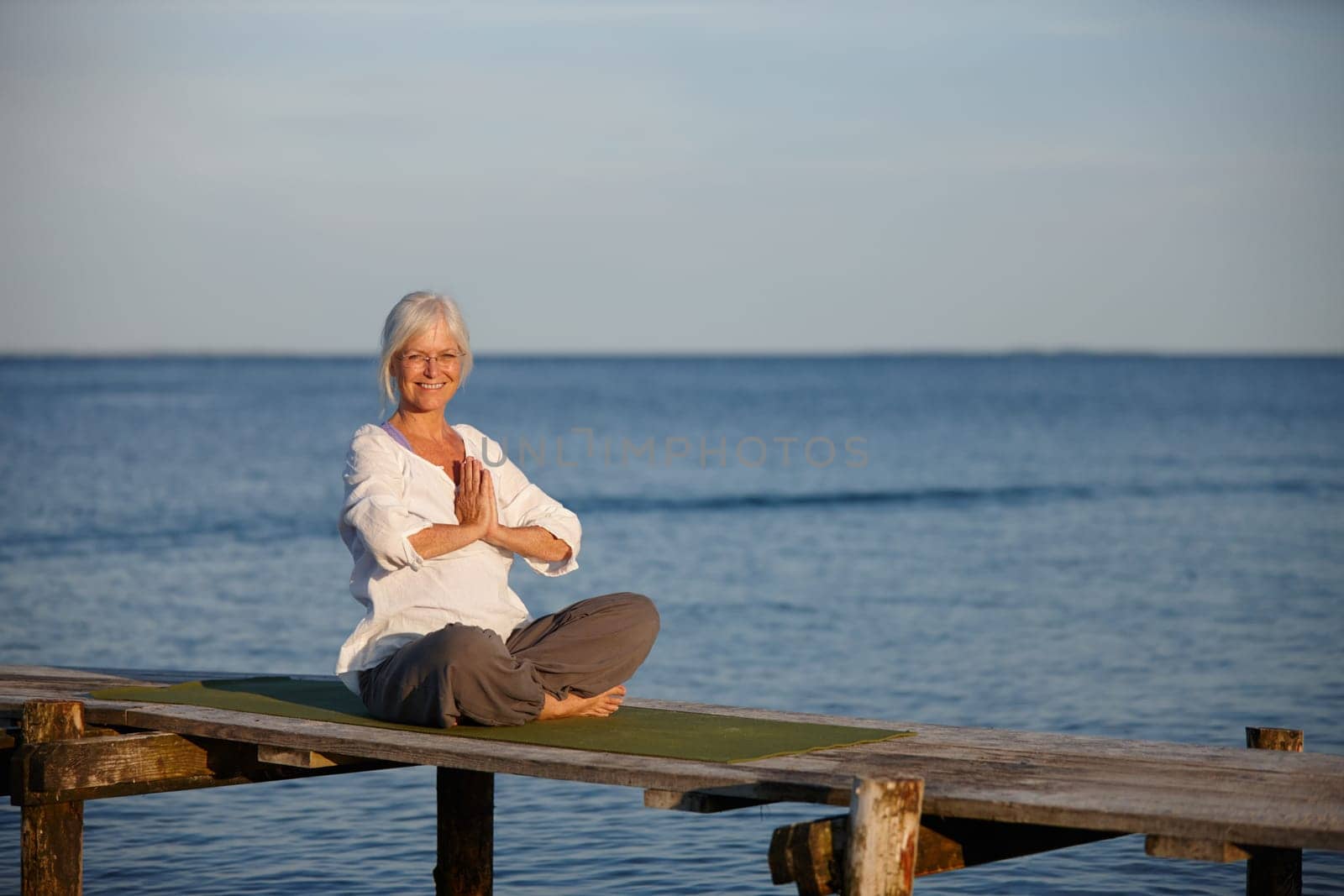 Yoga keeps me young at heart. Portrait of an attractive mature woman doing yoga on a pier out on the ocean. by YuriArcurs