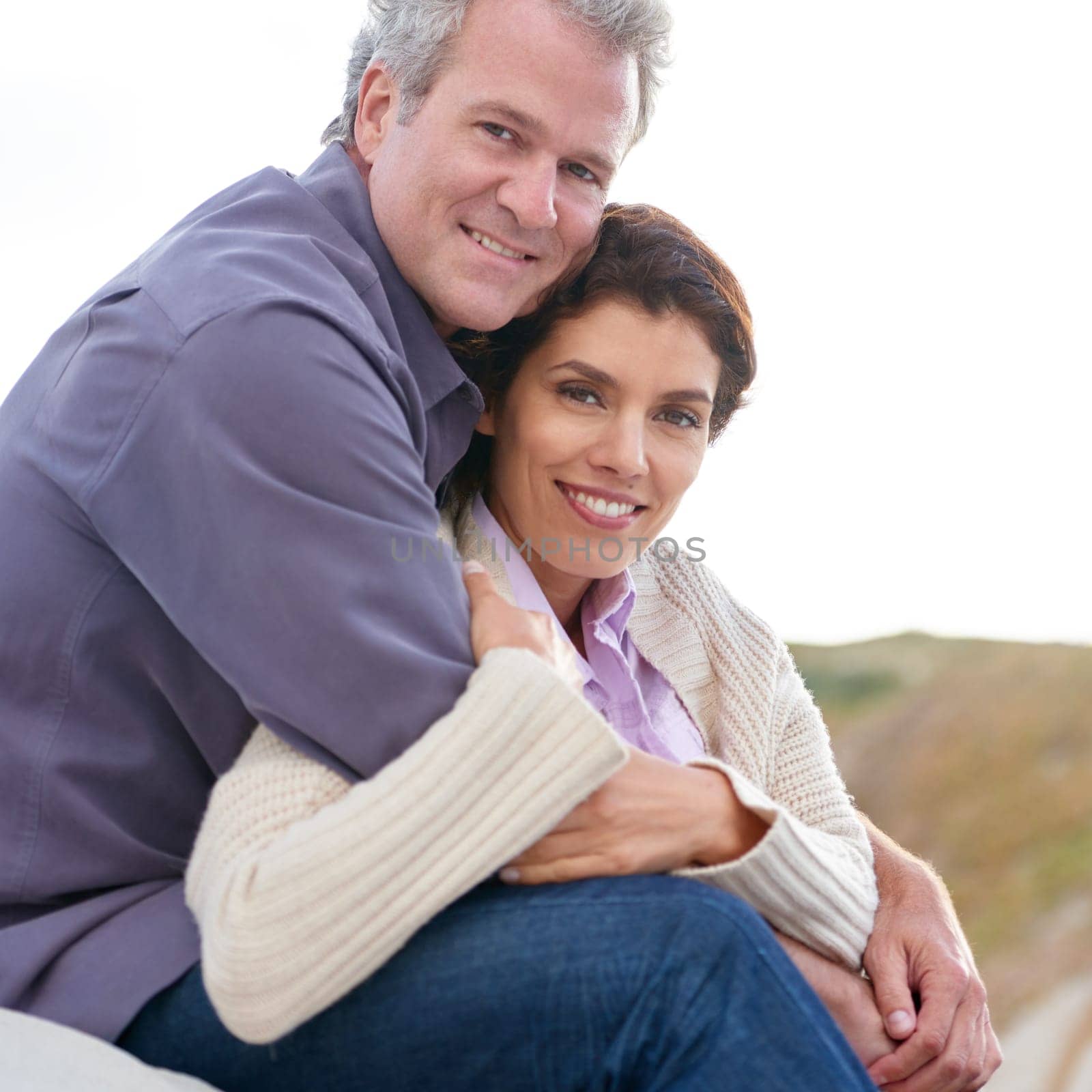 Appreciating one another. A mature couple hugging one another while sitting on a sand dune. by YuriArcurs