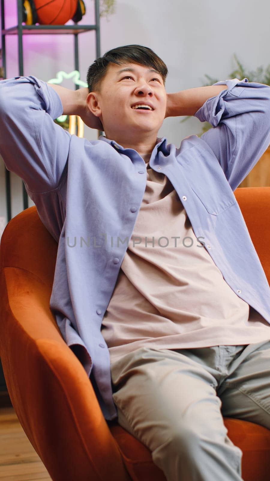 Tired asian man enjoy relaxing on home couch in room. Happy chinese guy lying on couch resting napping after hard working day, closed his eyes, put his hands behind his head stress free. Vertical shot