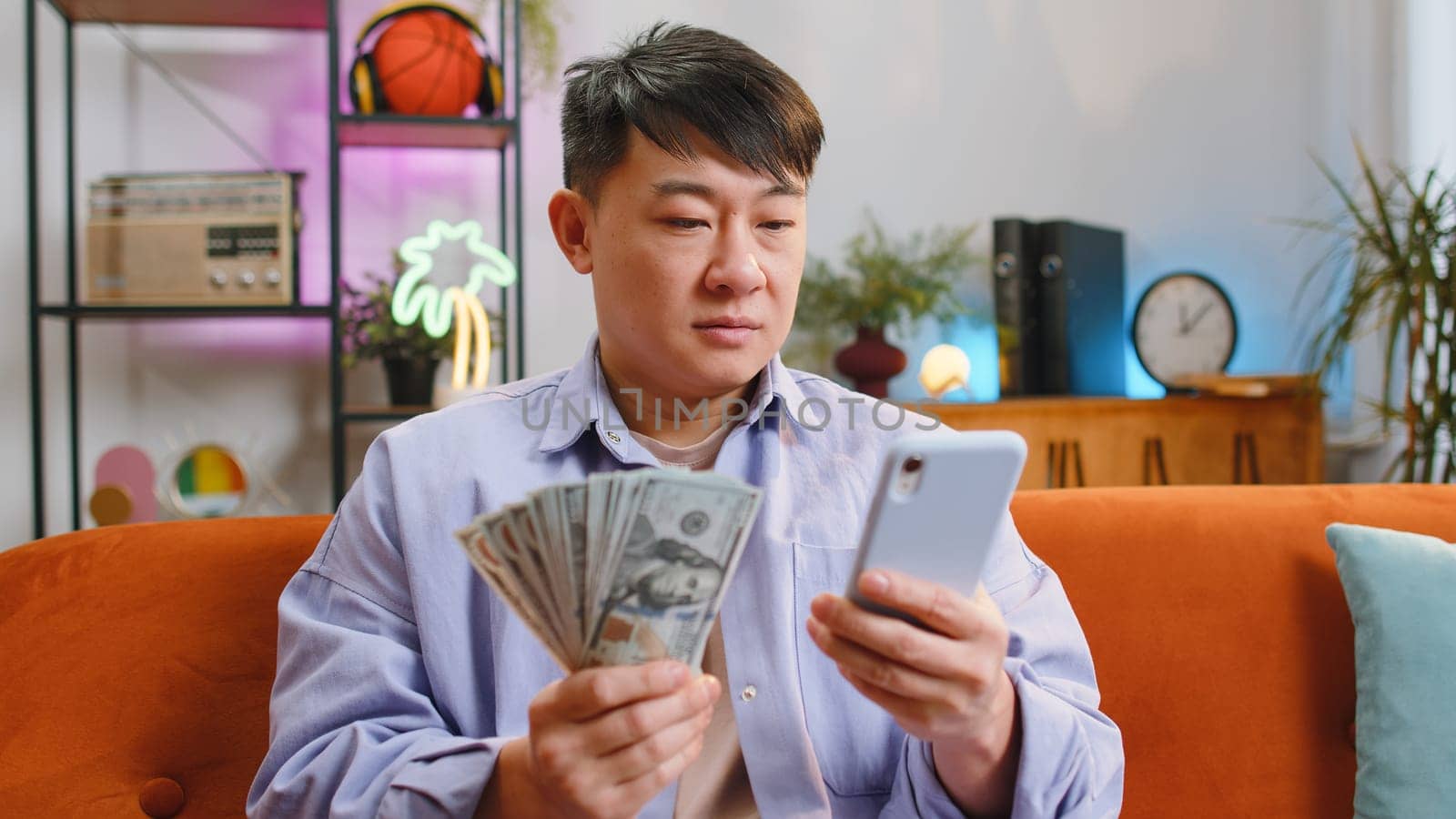 Smiling happy asian man counting money cash use smartphone, income saves lottery win, budget at home by efuror