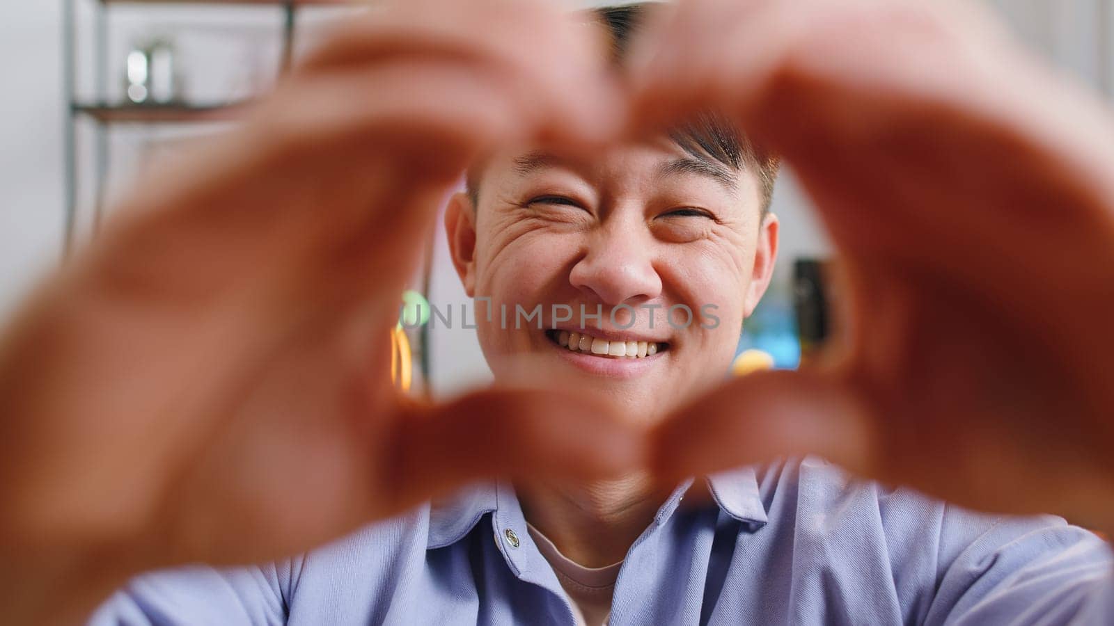 I love you. Happy asian man at home living room couch makes symbol of love, showing heart sign to camera, express romantic feelings express sincere positive feelings. Charity, gratitude, donation