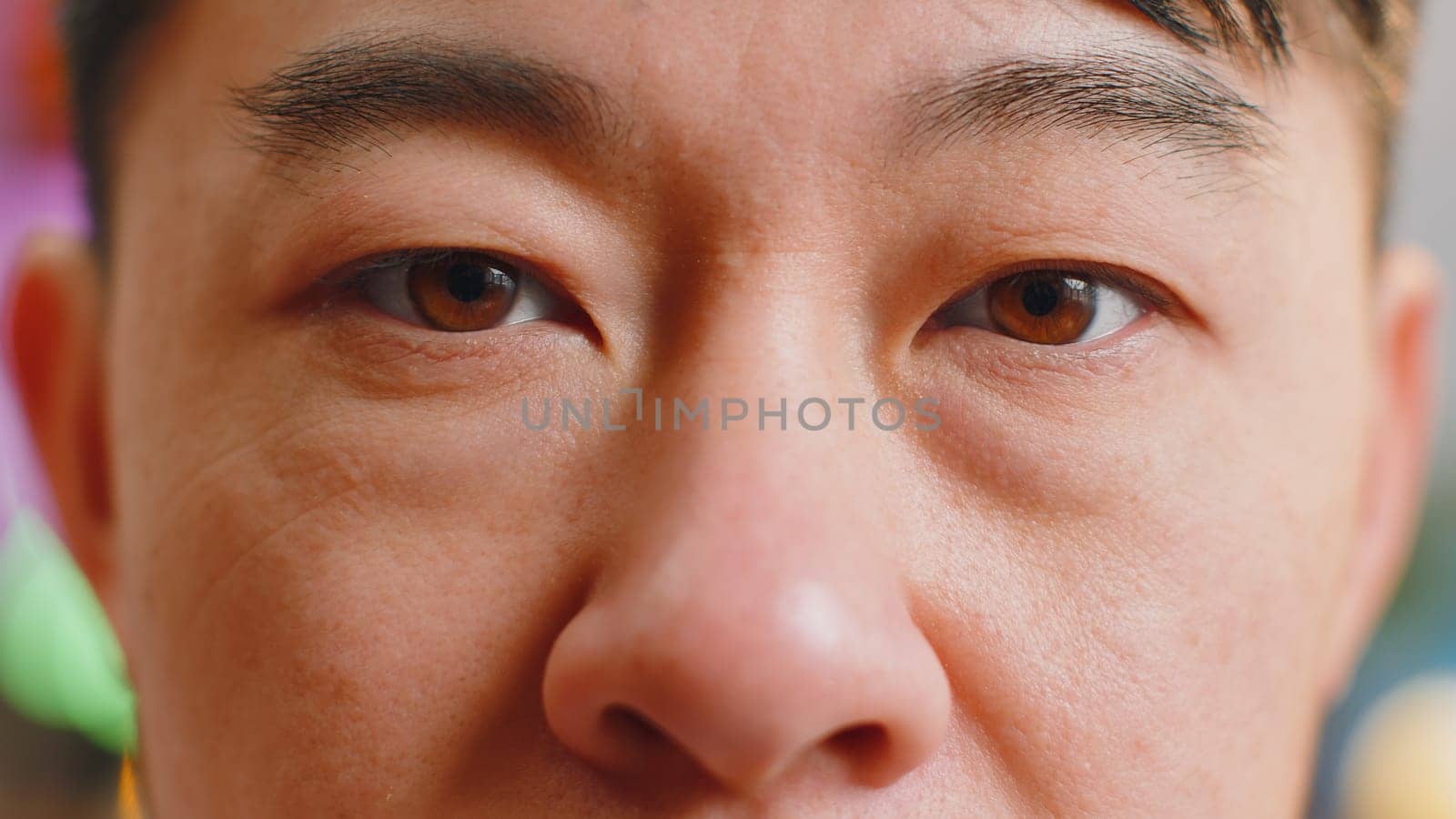 Extreme close-up macro portrait of smiling asian man face. Middle-aged guy eyes looking at camera. Adult positive chinese man opening wide his closed eyes. Brown eyes of brunette male attractive model