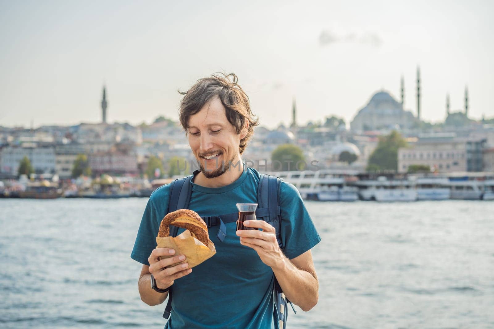 Man in Istanbul having breakfast with Simit and a glass of Turkish tea. Glass of Turkish tea and bagel Simit against golden horn bay in Istanbul, Turkey. Turkiye.