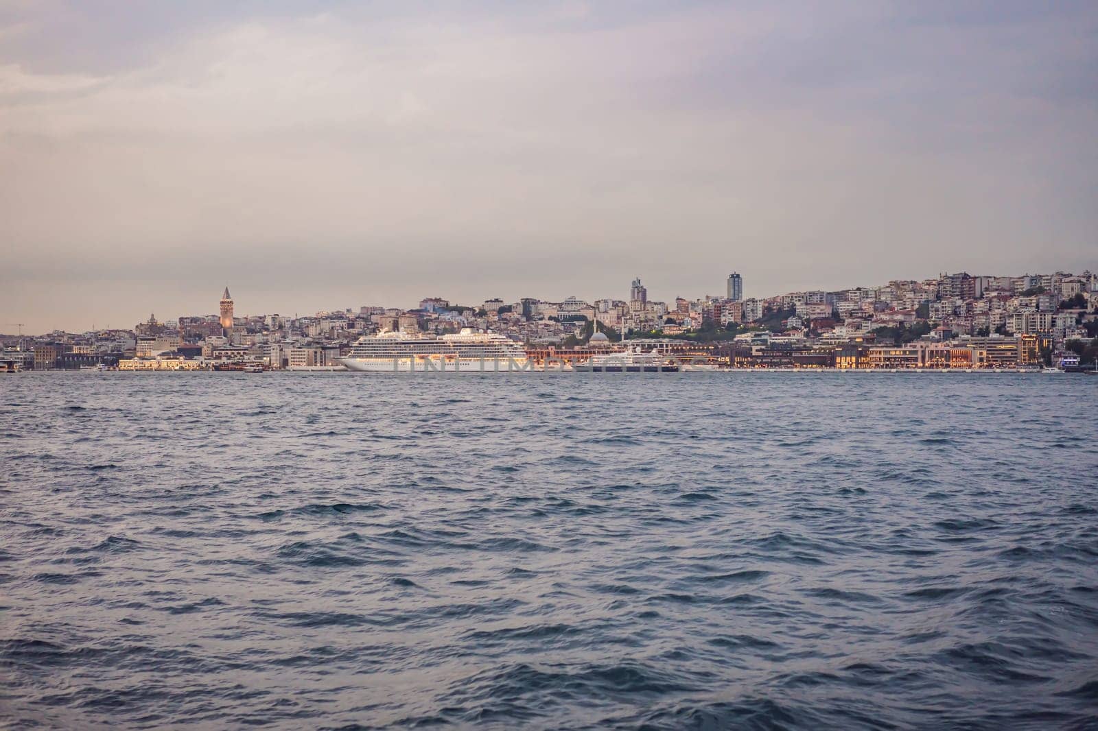 Huge cruise ship docked at terminal of Galataport, located along shore of Bosphorus strait, in Karakoy neighbourhood, with Galata tower in the background by galitskaya