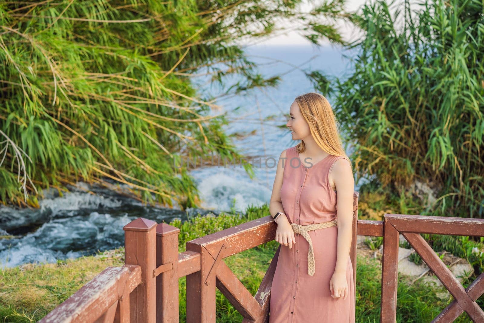 Beautiful woman with long hair on the background of Duden waterfall in Antalya. Famous places of Turkey. Lower Duden Falls drop off a rocky cliff falling from about 40 m into the Mediterranean Sea in amazing water clouds. Tourism and travel destination photo in Antalya, Turkey. Turkiye.