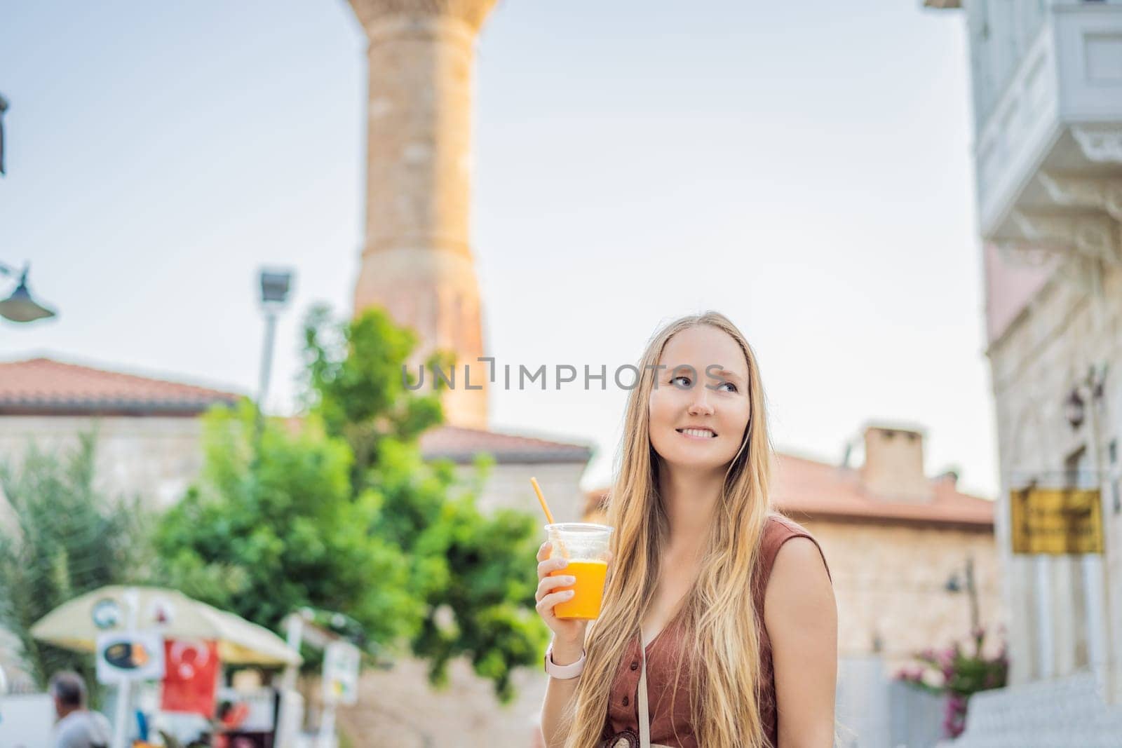 Happy woman tourist with fresh juice on background of old street of Antalya. female tourist traveler discover interesting places and popular attractions and walks in the old city Kalechi of Antalya, Turkey. Turkiye.