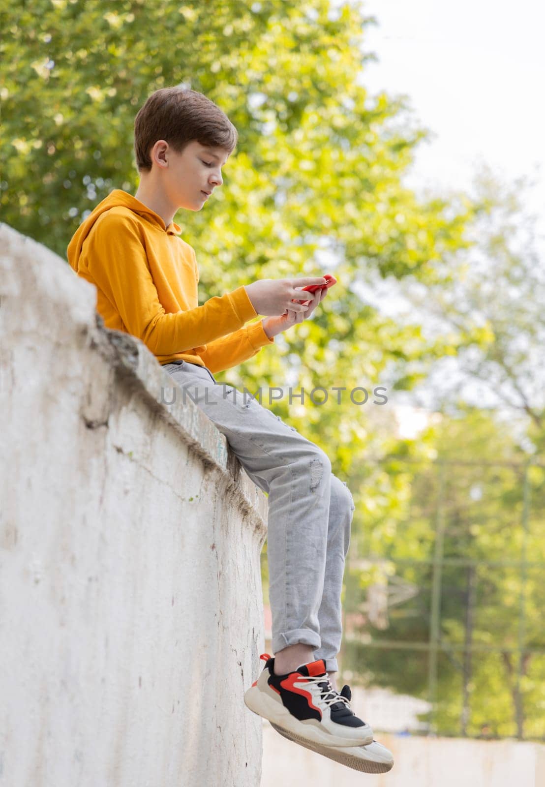 Thoughtful teenager boy resting. Holding and using a smartphone for networking on a sunny day, outdoors. by Ri6ka