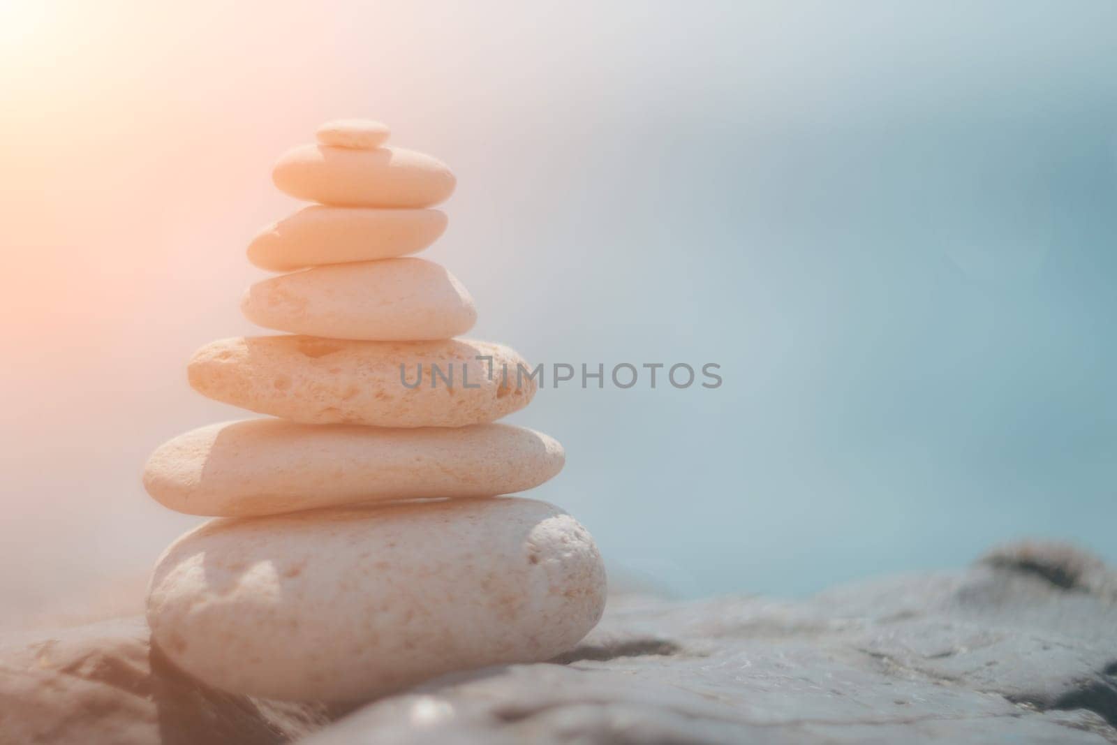 Balanced Pebbles Pyramid on the Beach on Sunny Day and Clear Sky at Sunset. Blue Sea on Background Selective focus, zen stones on sea beach, meditation, spa, harmony, calm, balance concept.