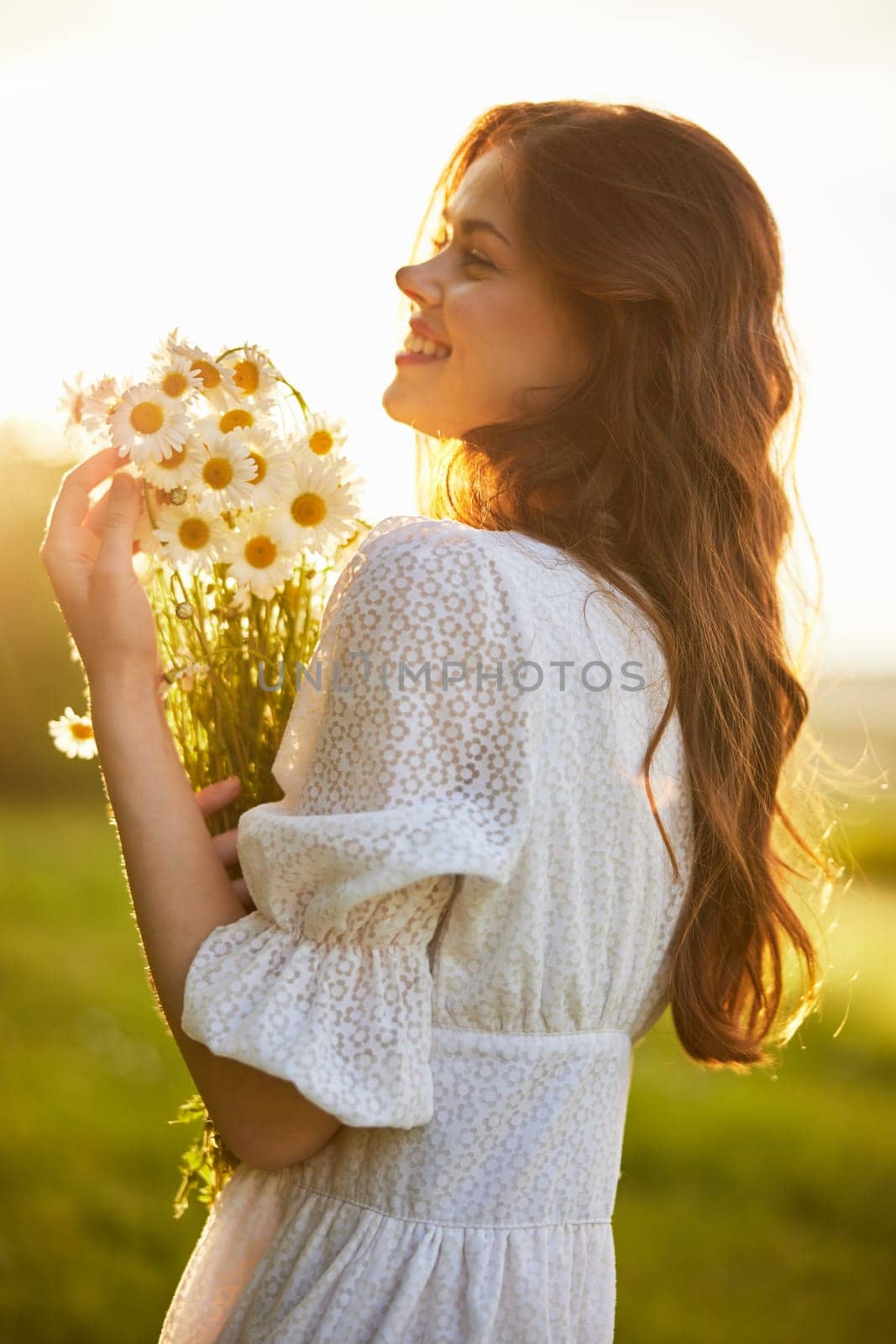 portrait of a woman in a light dress in a field during sunset with a bouquet of daisies in her hands. High quality photo