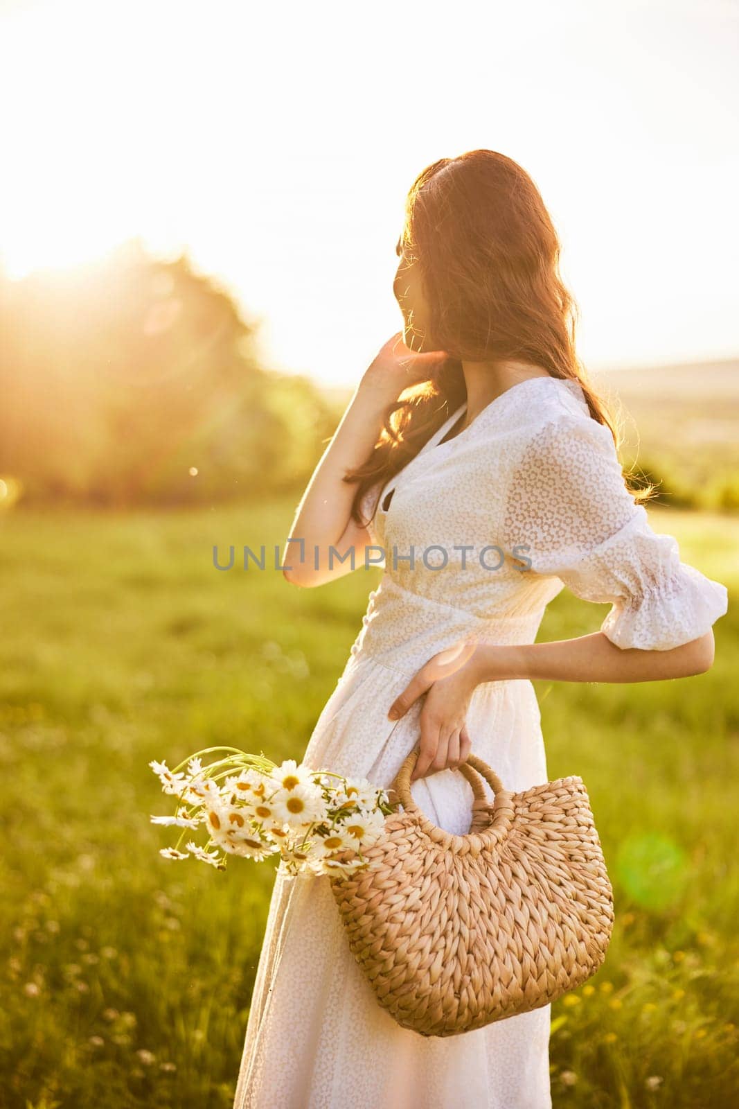 girl in a light summer dress with a basket of flowers in her hands with glare from the setting sun. High quality photo