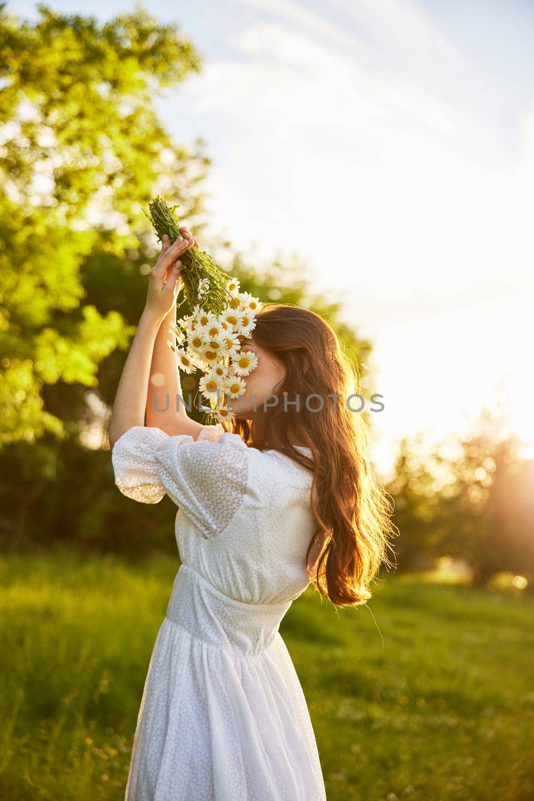 vertical portrait of a red-haired woman in nature during sunset sniffing a bouquet of daisies. High quality photo