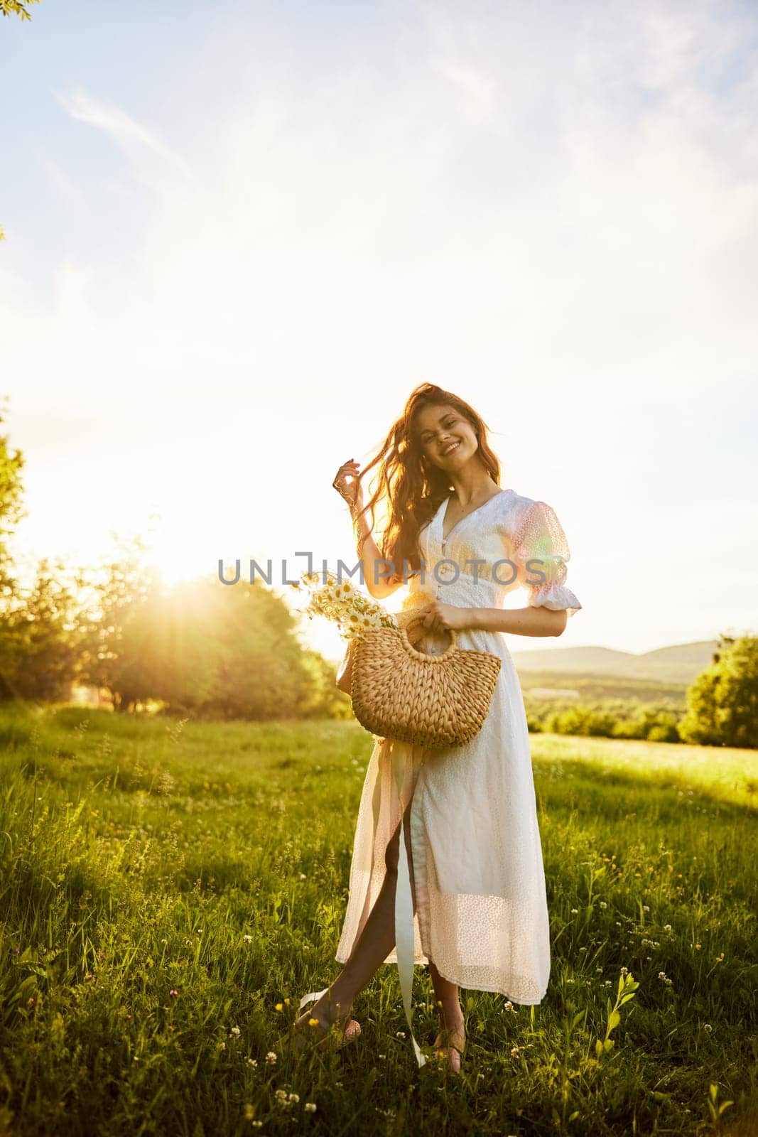 a woman in a long, light dress stands in a chamomile field at sunset. full length photo by Vichizh