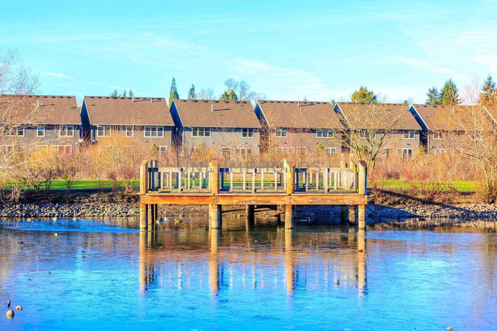 A small wooden deck at the lake shore, with residence buildings in the back ground.
