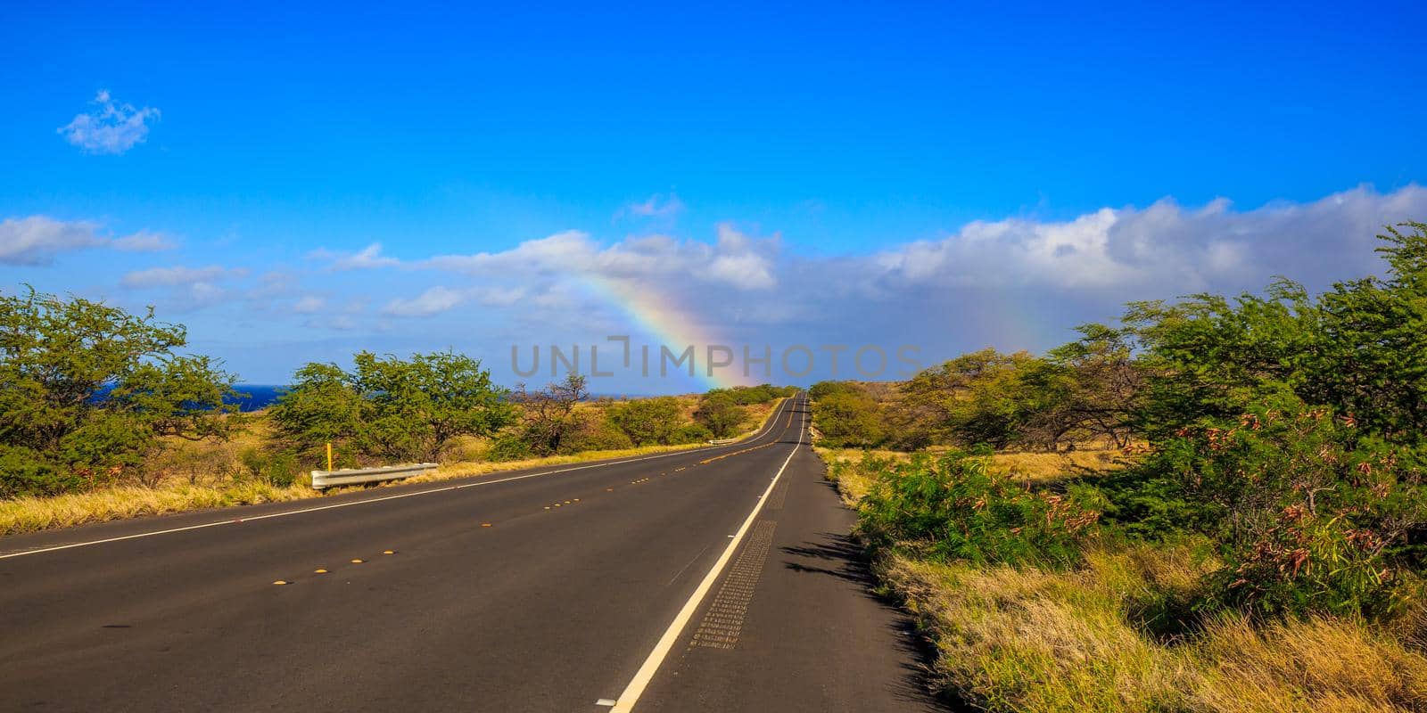 Partial rainbow appears at the end of the highway road, under the sun.