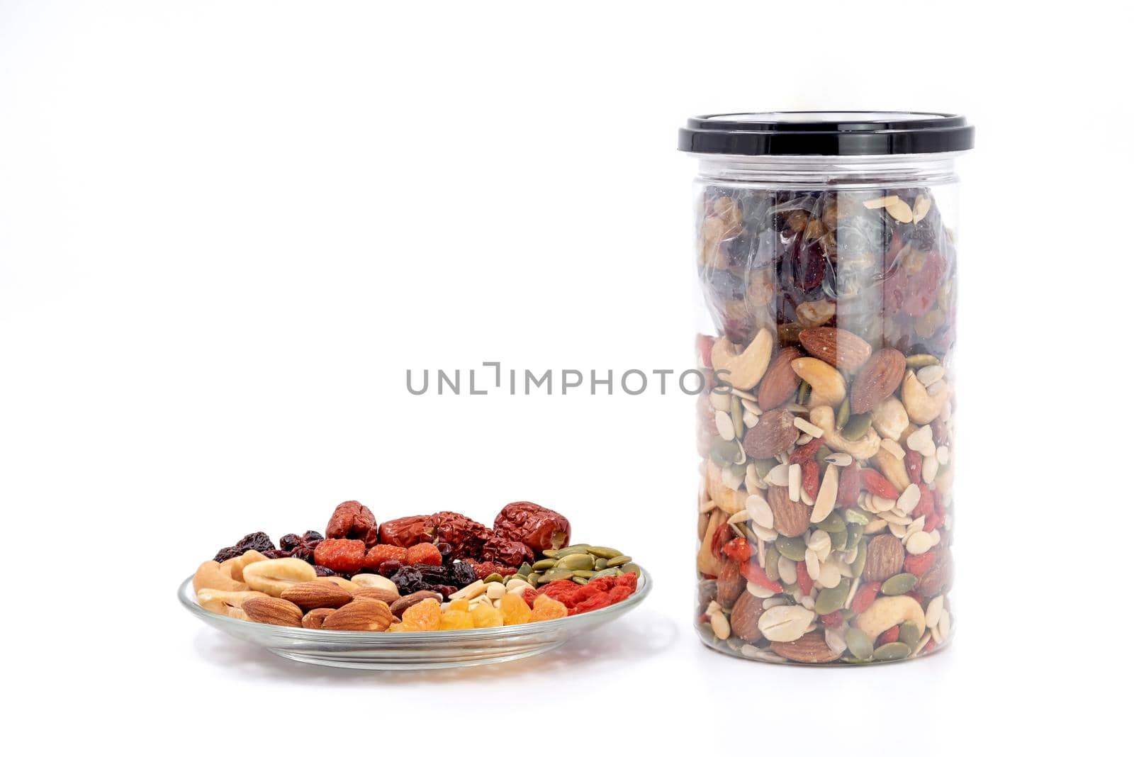 Whole grains and dried fruit in a glass plate and plastic bottle isolated on white background.
