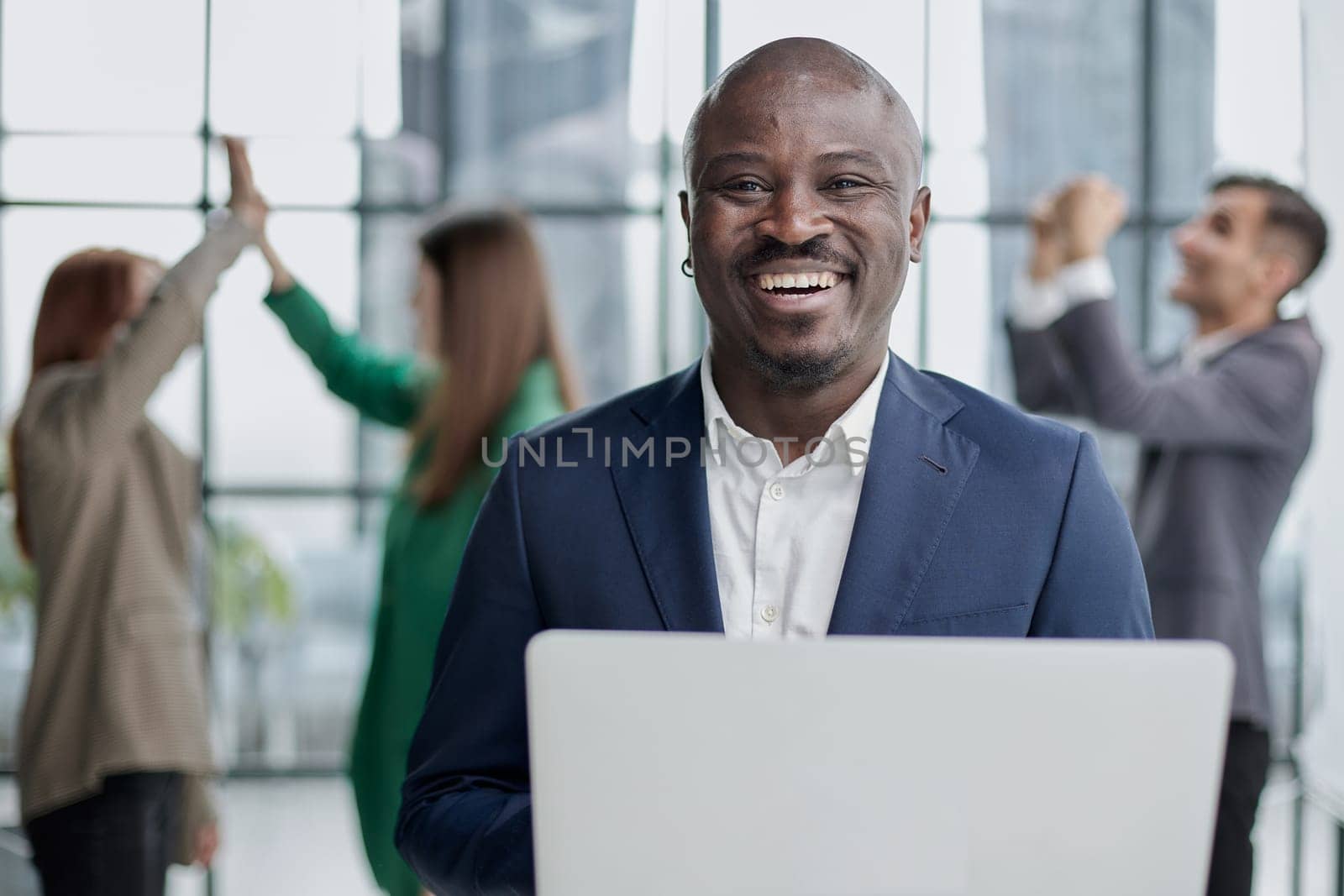 Young African American man in a business suit holding a laptop against the background of his colleagues