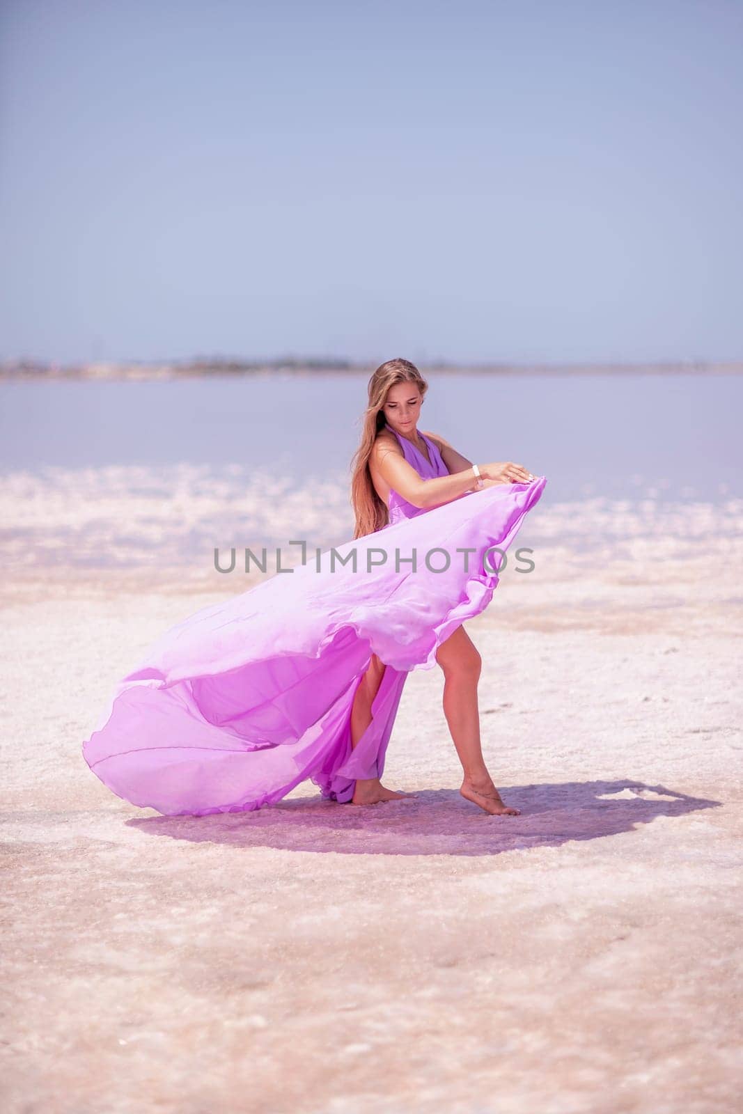 Woman pink salt lake. Against the backdrop of a pink salt lake, a woman in a long pink dress takes a leisurely stroll along the white, salty shore, capturing a wanderlust moment