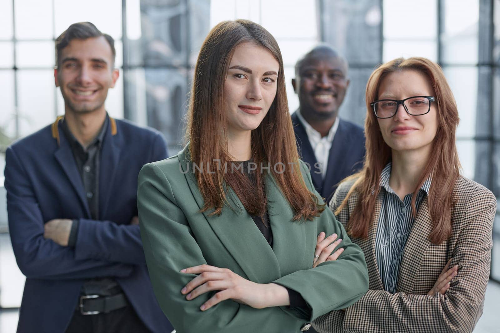 Young executive smiling and standing in a bright room with her team behind her by Prosto