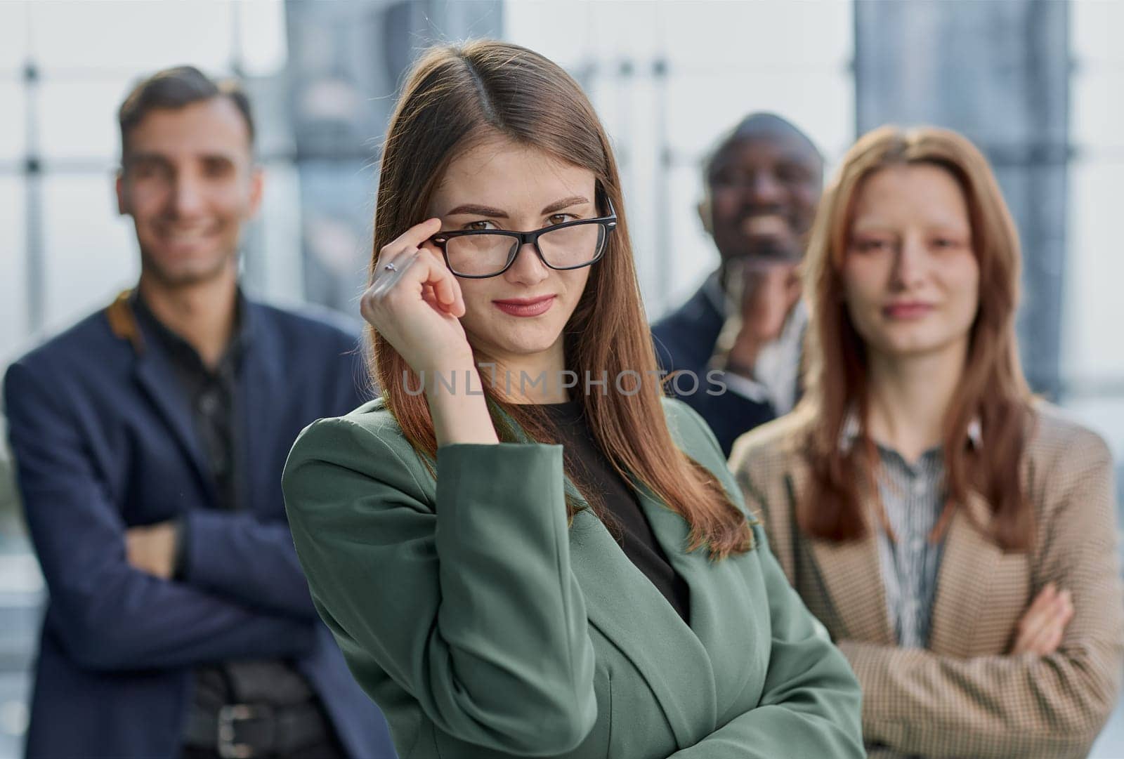 Young executive smiling and standing in a bright room with her team behind her