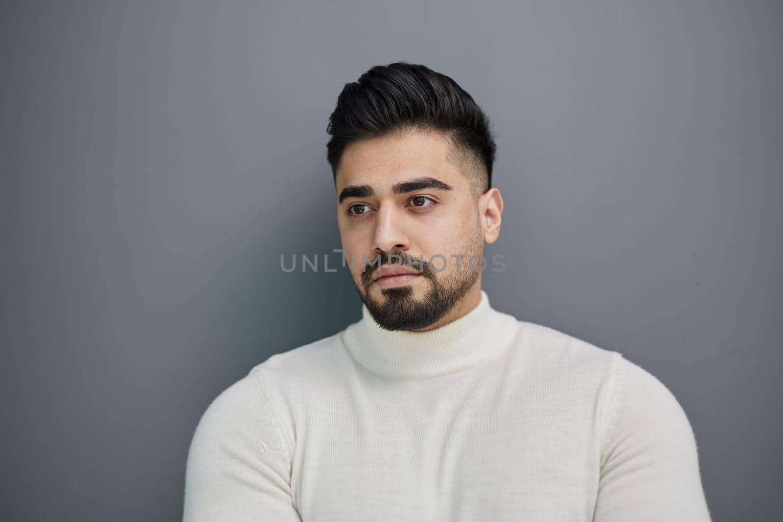 Portrait of a stylish man posing on a gray background with his arms crossed