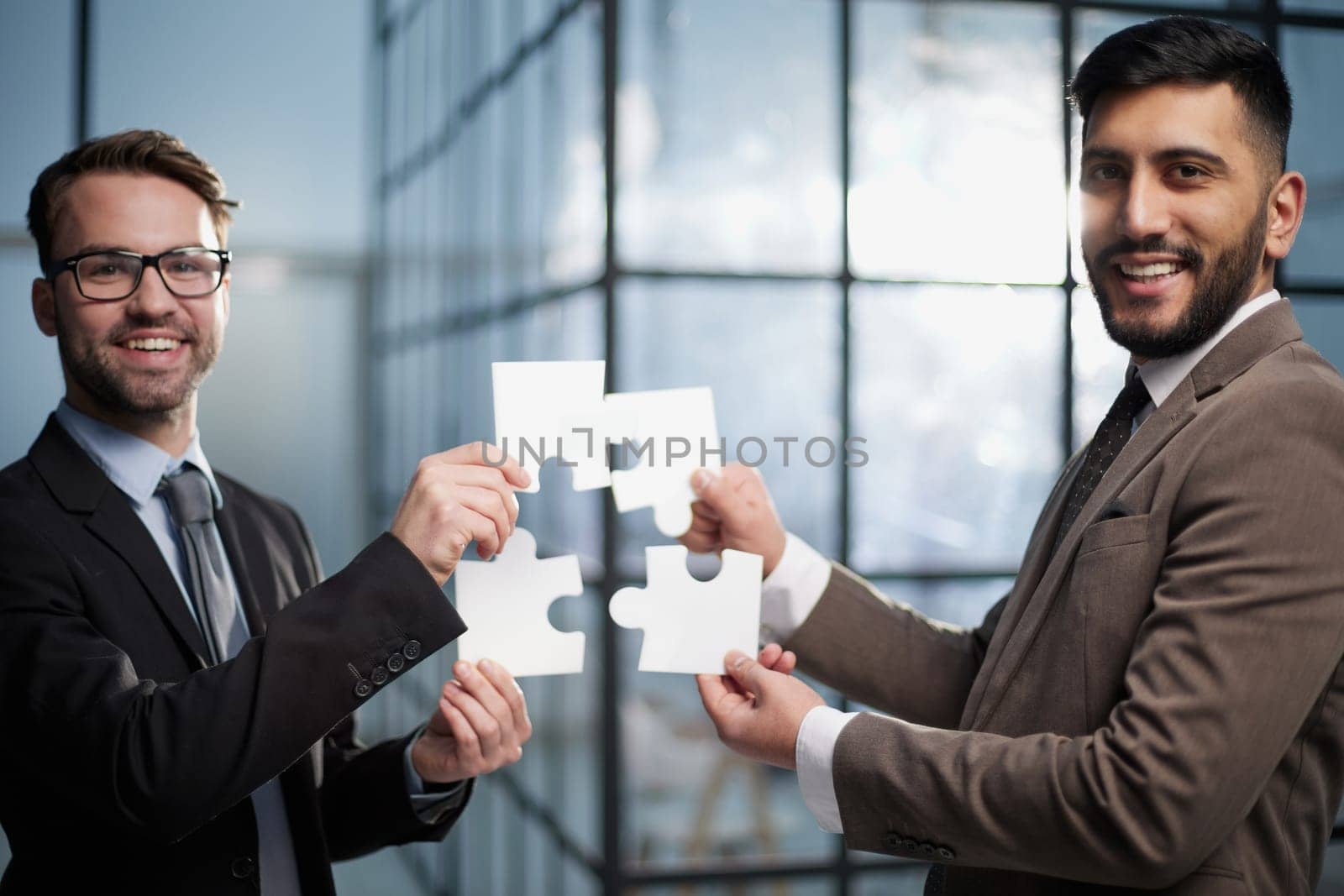 two businessmen put together a puzzle opposite each other on the background of the office