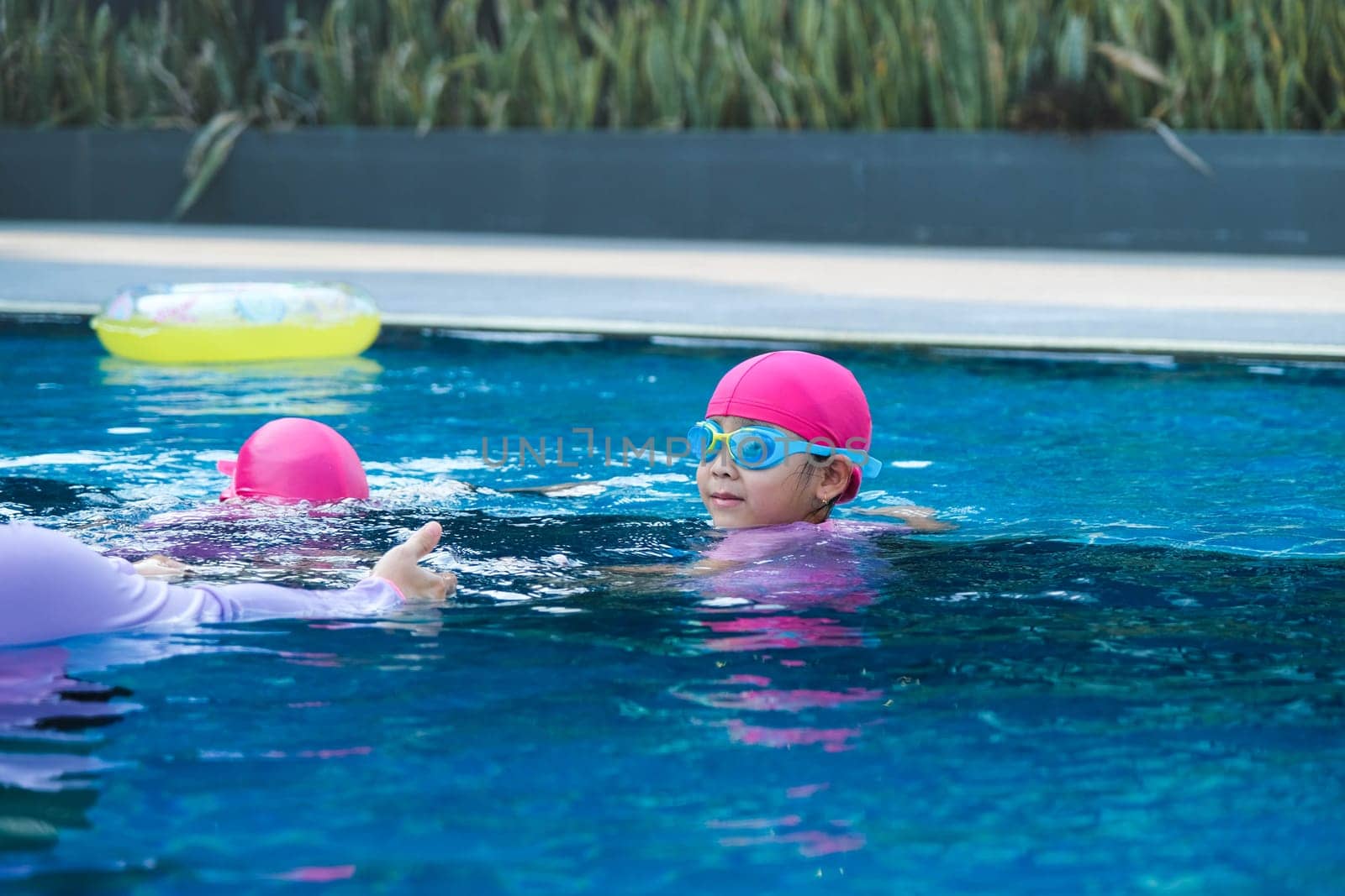 Little girl practicing swimming in the pool. Happy children swimming and playing in the water. summer vacation concept. by TEERASAK