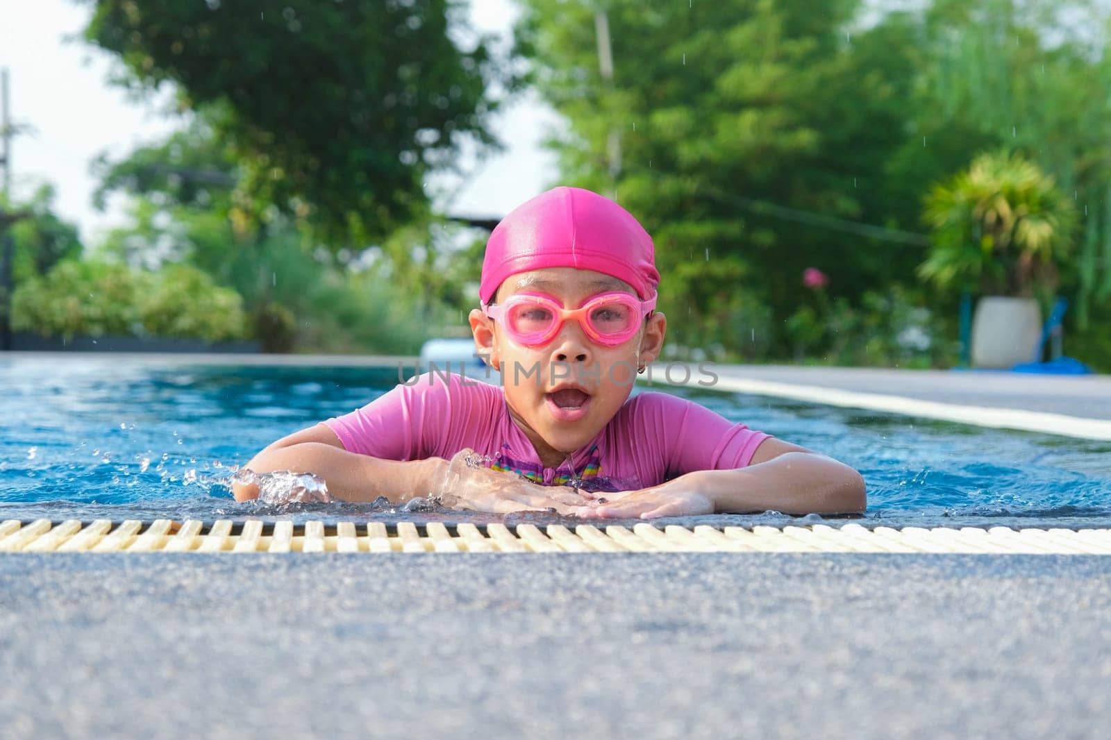 Cute girl with swimming goggles in the swimming pool. Little girl swimming and playing in the water. summer vacation concept.