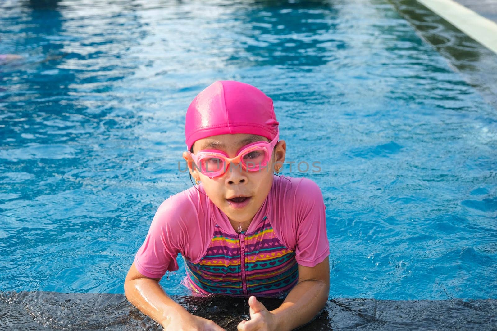 Cute girl with swimming goggles in the swimming pool. Little girl swimming and playing in the water. summer vacation concept.