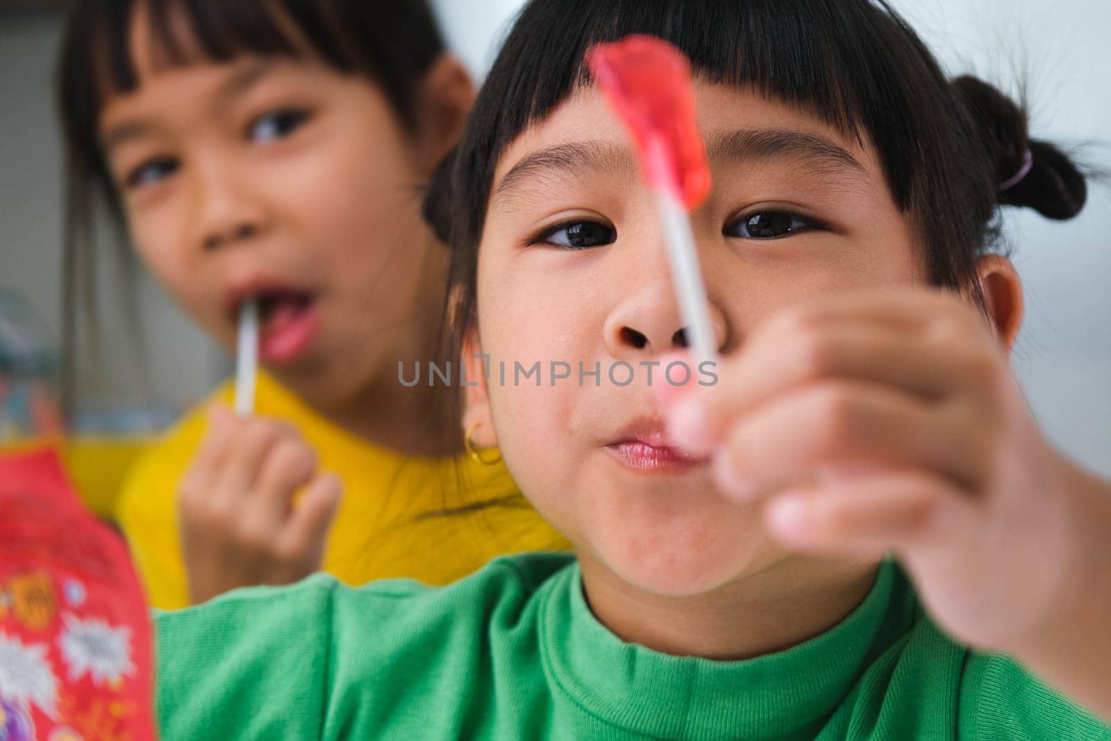 Two happy cute little girls eating lollipops. Funny kid with lollipop candy. Child eating sweets. by TEERASAK